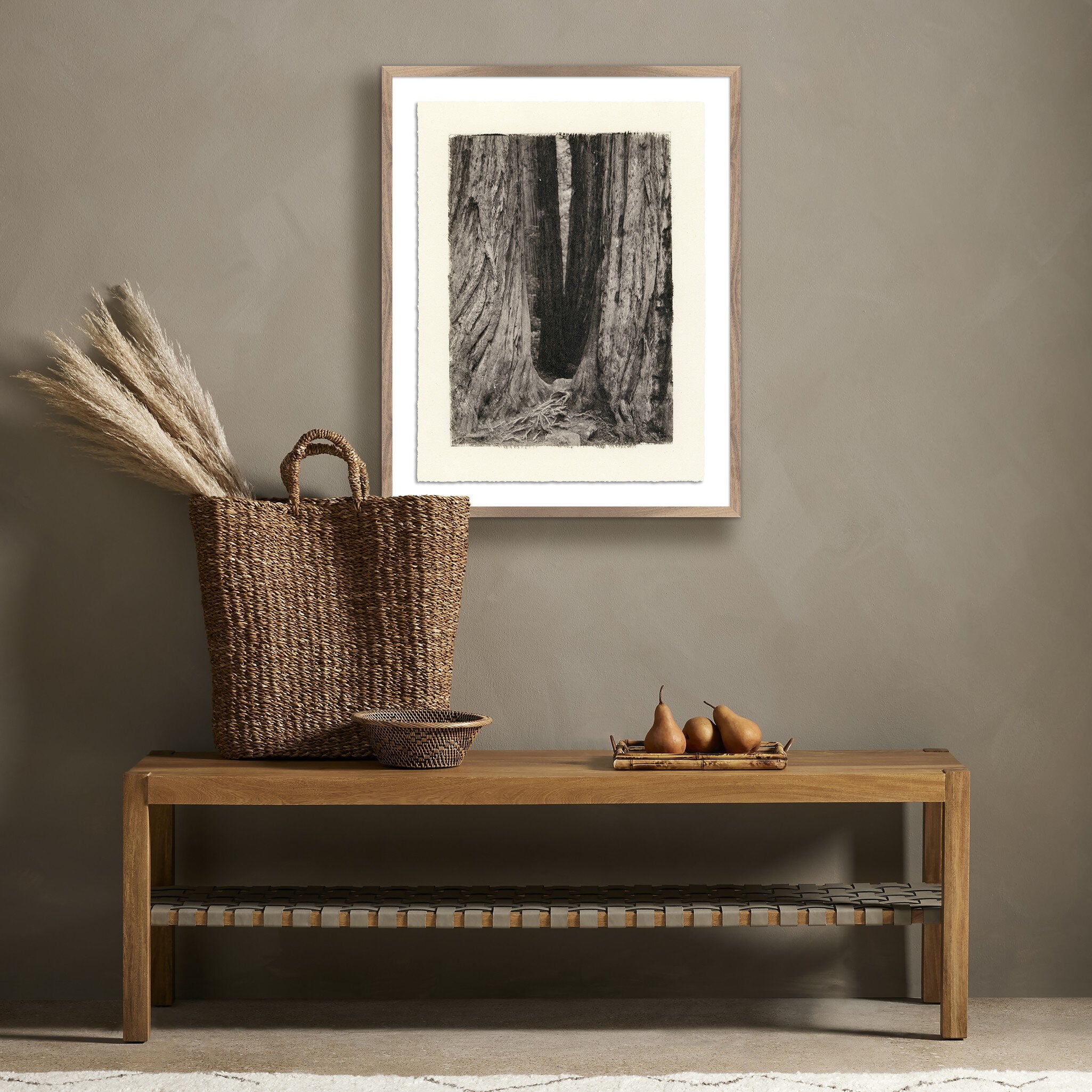 Wooden bench with woven basket and decorative items against a wall with framed artwork.