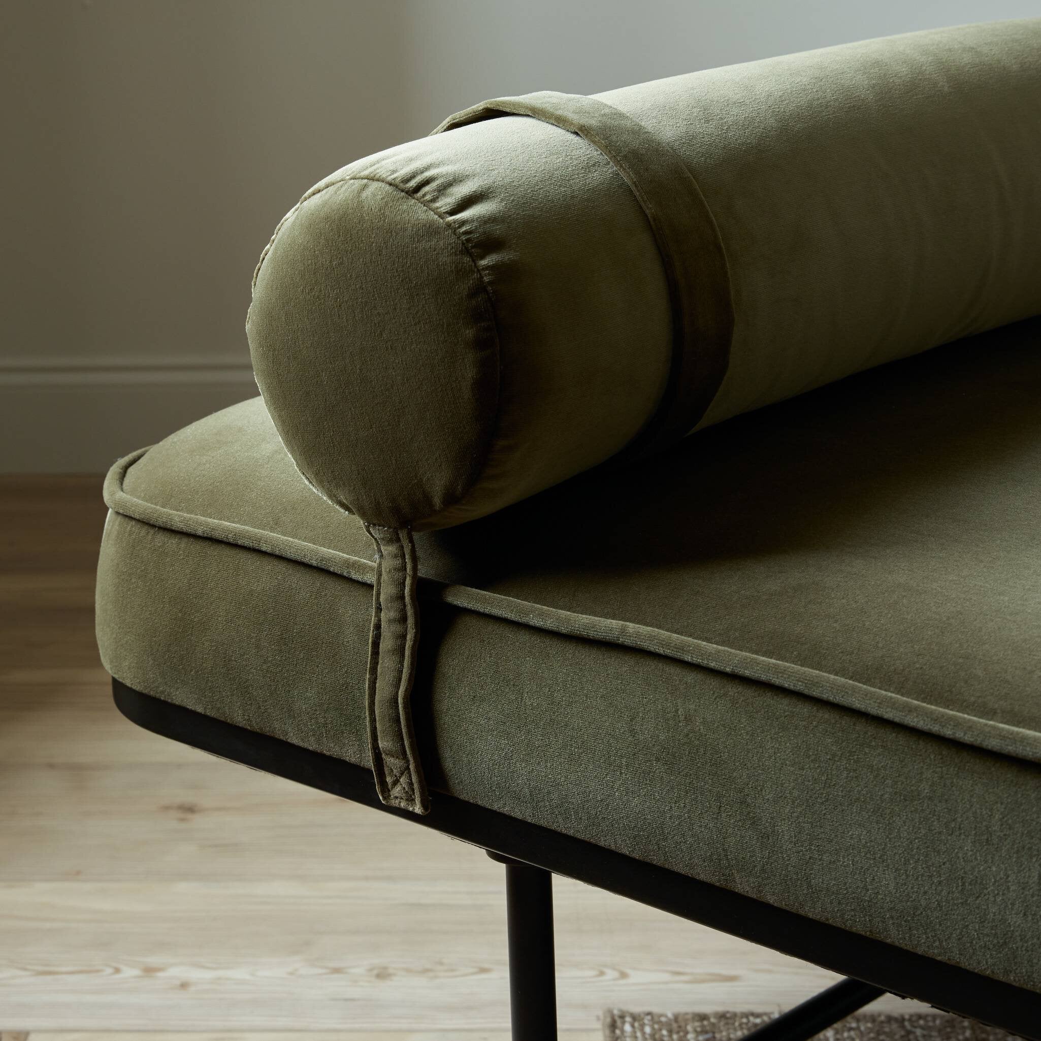 Green chaise with a wooden floor and neutral wall in the background