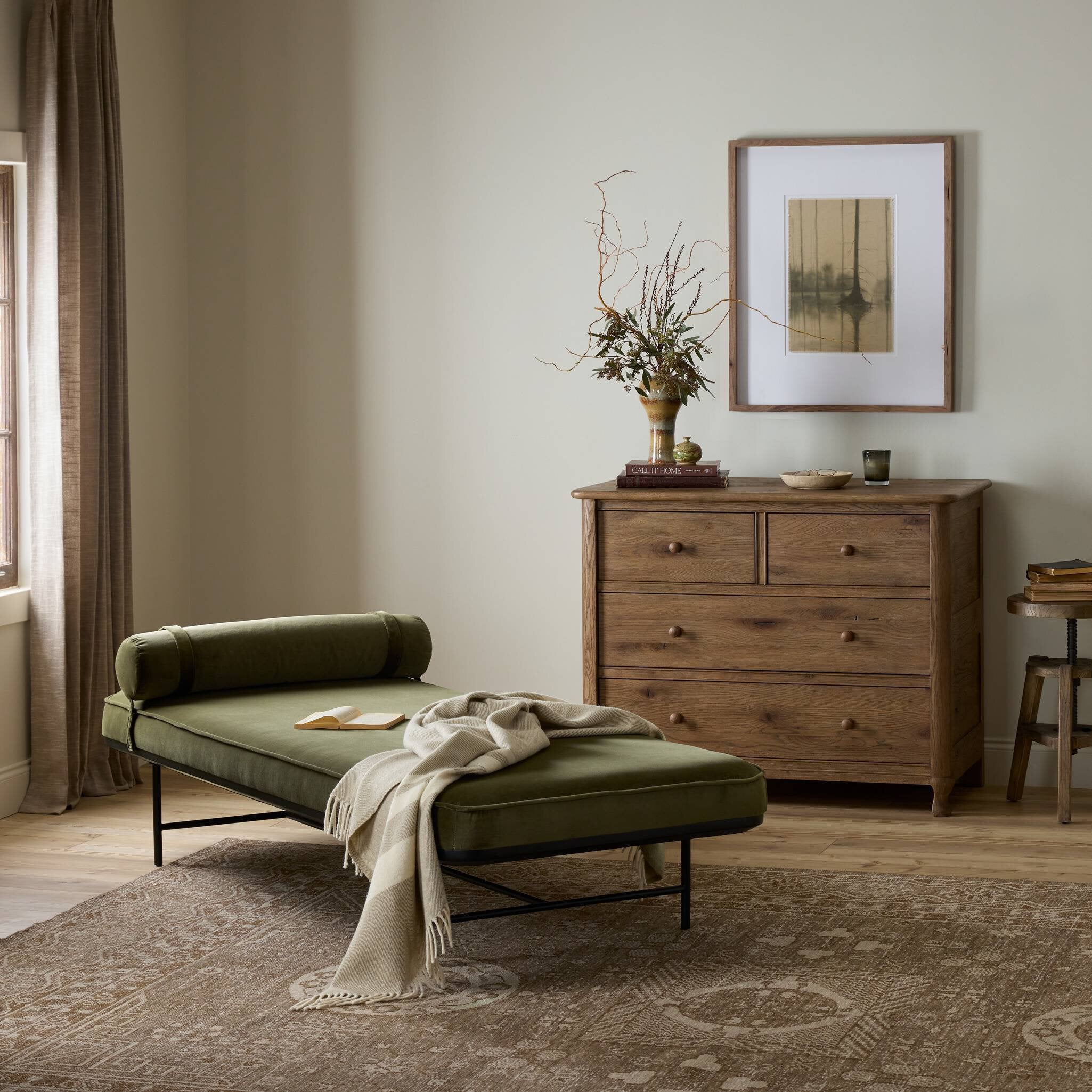 Green daybed in a room with wooden dresser and framed picture