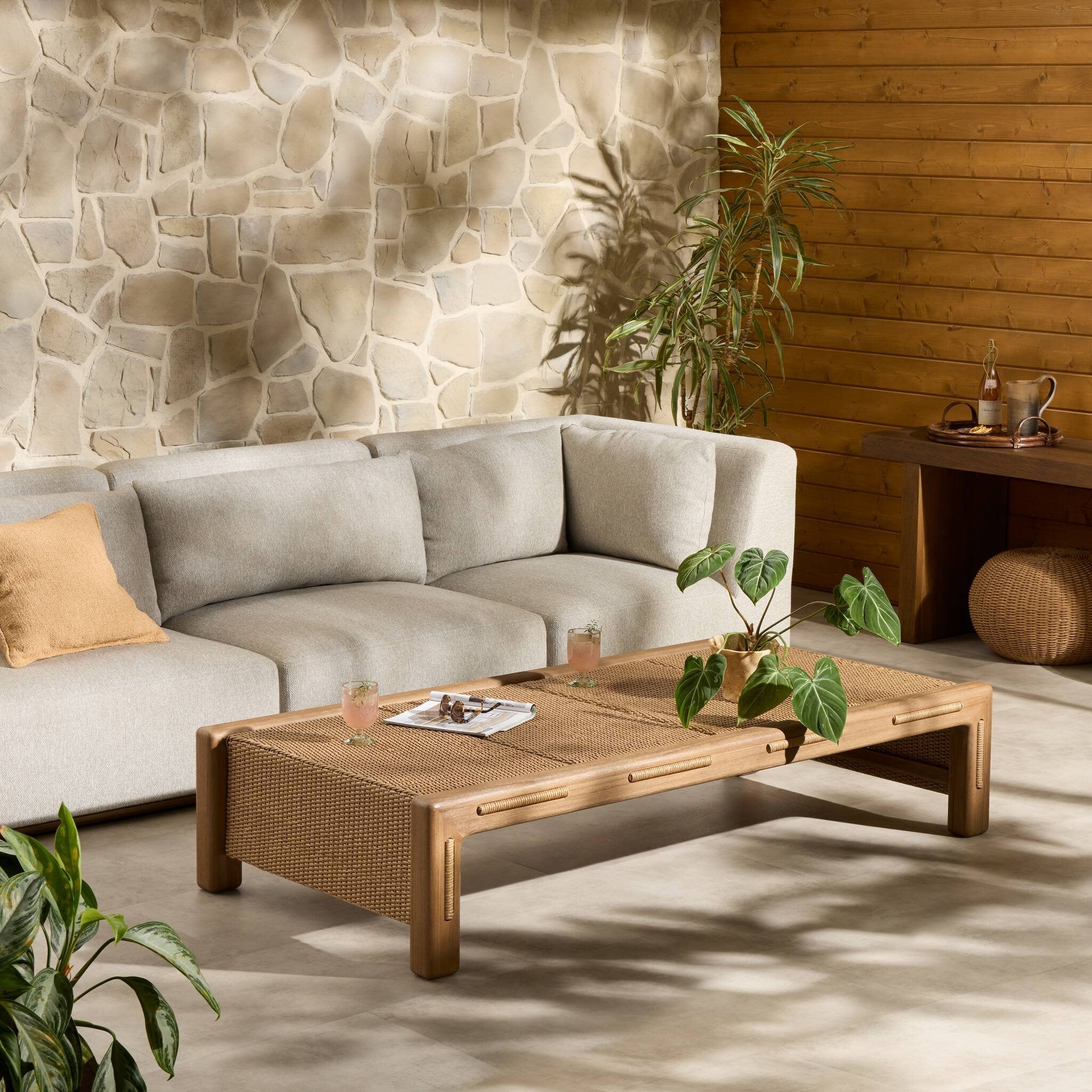 Modern outdoor iving room with a stone wall, wooden coffee table, and sectional sofa.