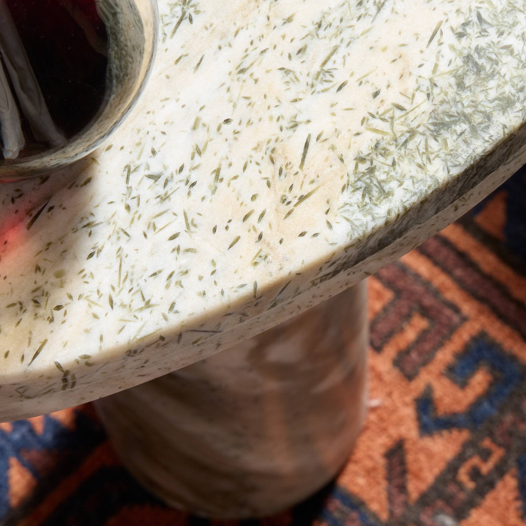 Close-up of a textured end table surface with a cup on top, on a patterned rug.
