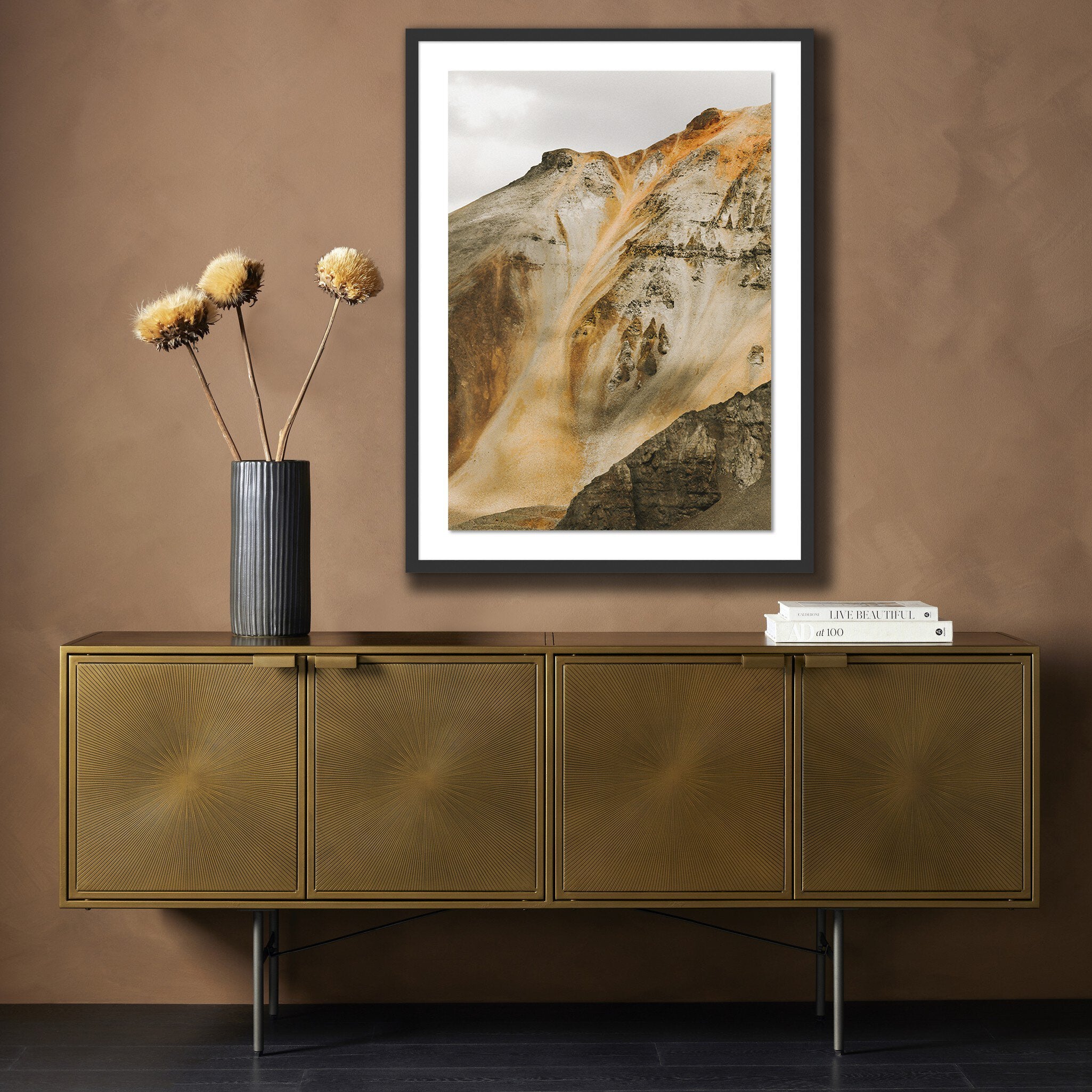 Gold sideboard with a vase of flowers and framed abstract art on a brown wall.