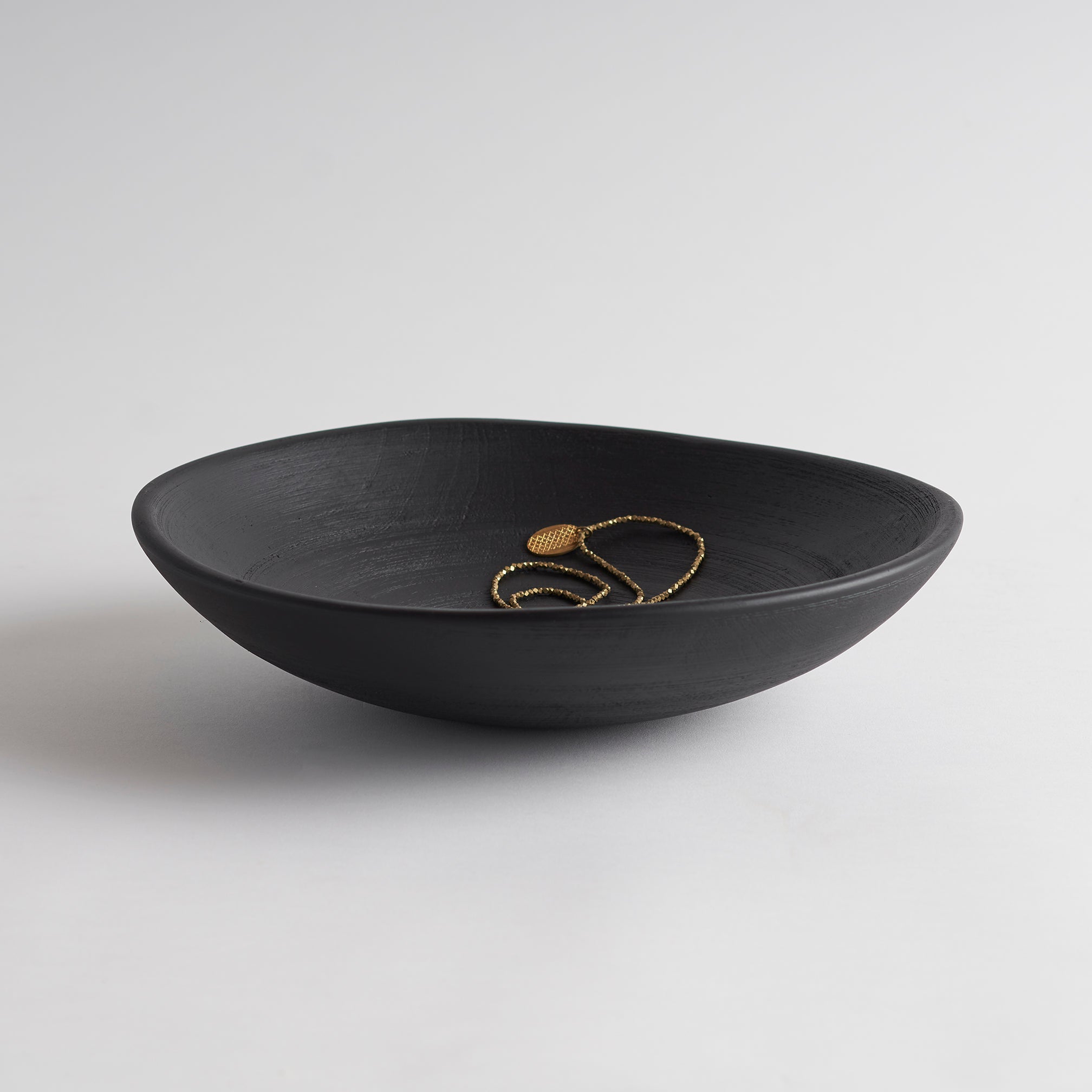 Black bowl with gold jewelry on a white background