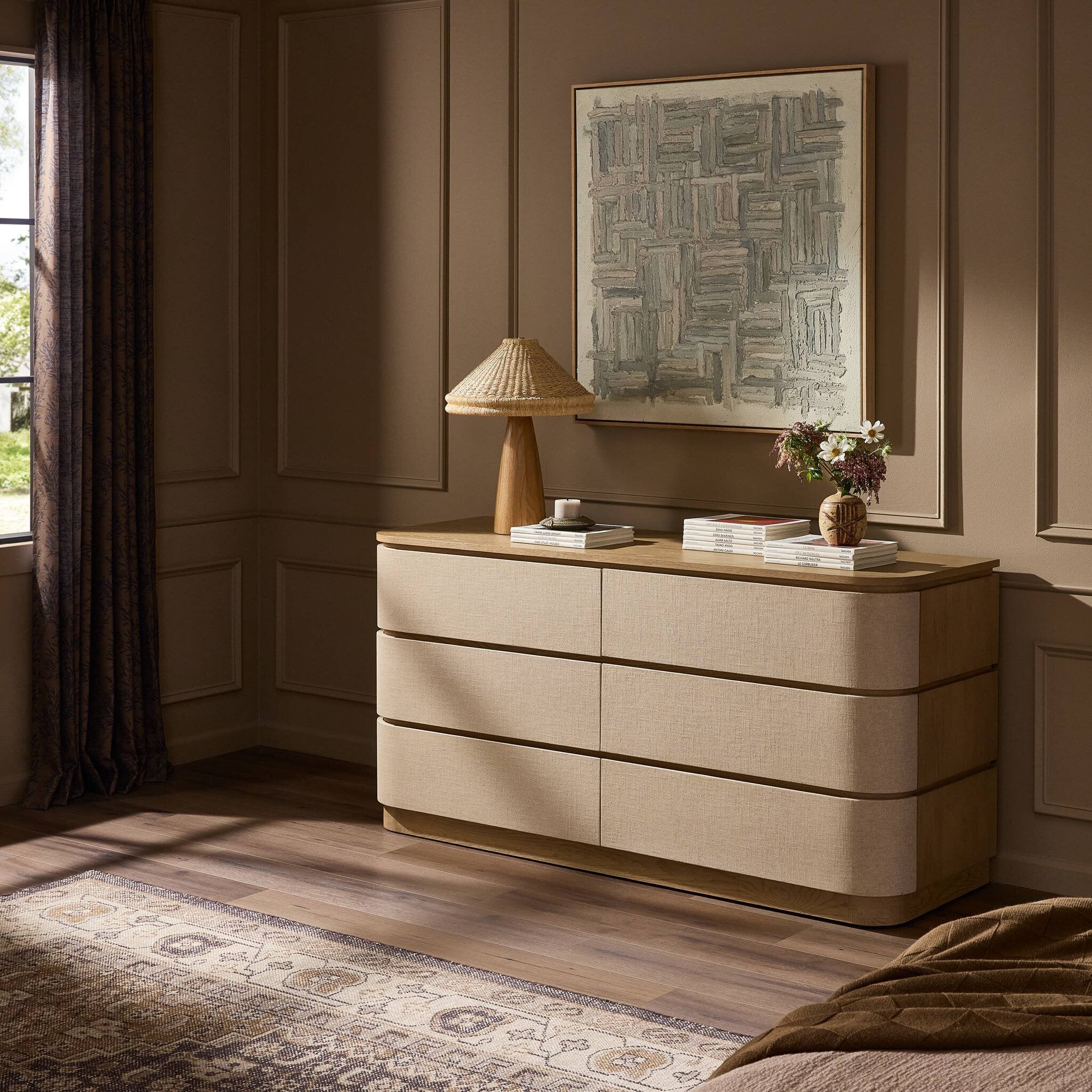 Beige dresser with decorative items in a room with a painting on the wall.