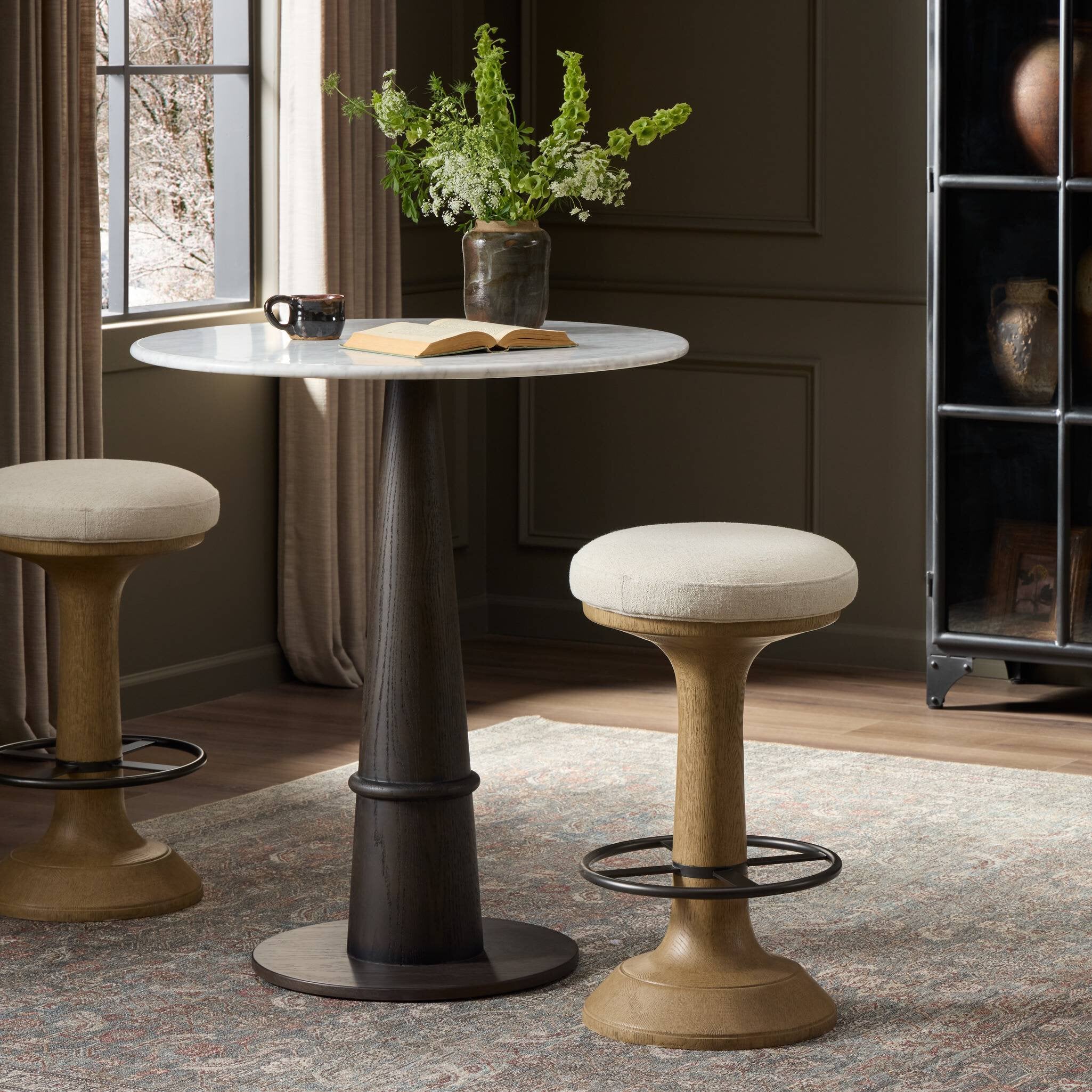 Round table with stools in a room with a window and bookshelf.