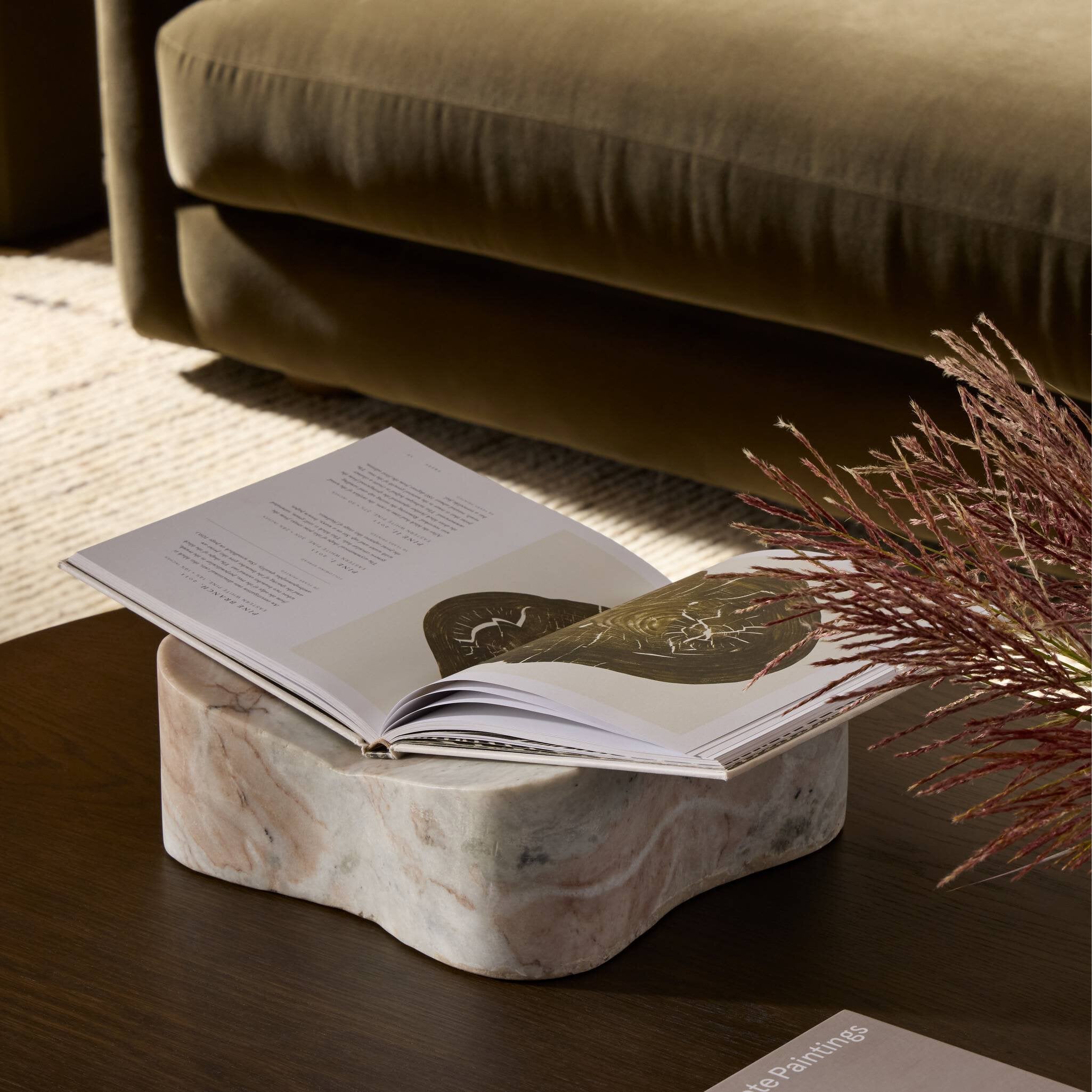 Open book on a marble holder with a plant and sofa in the background