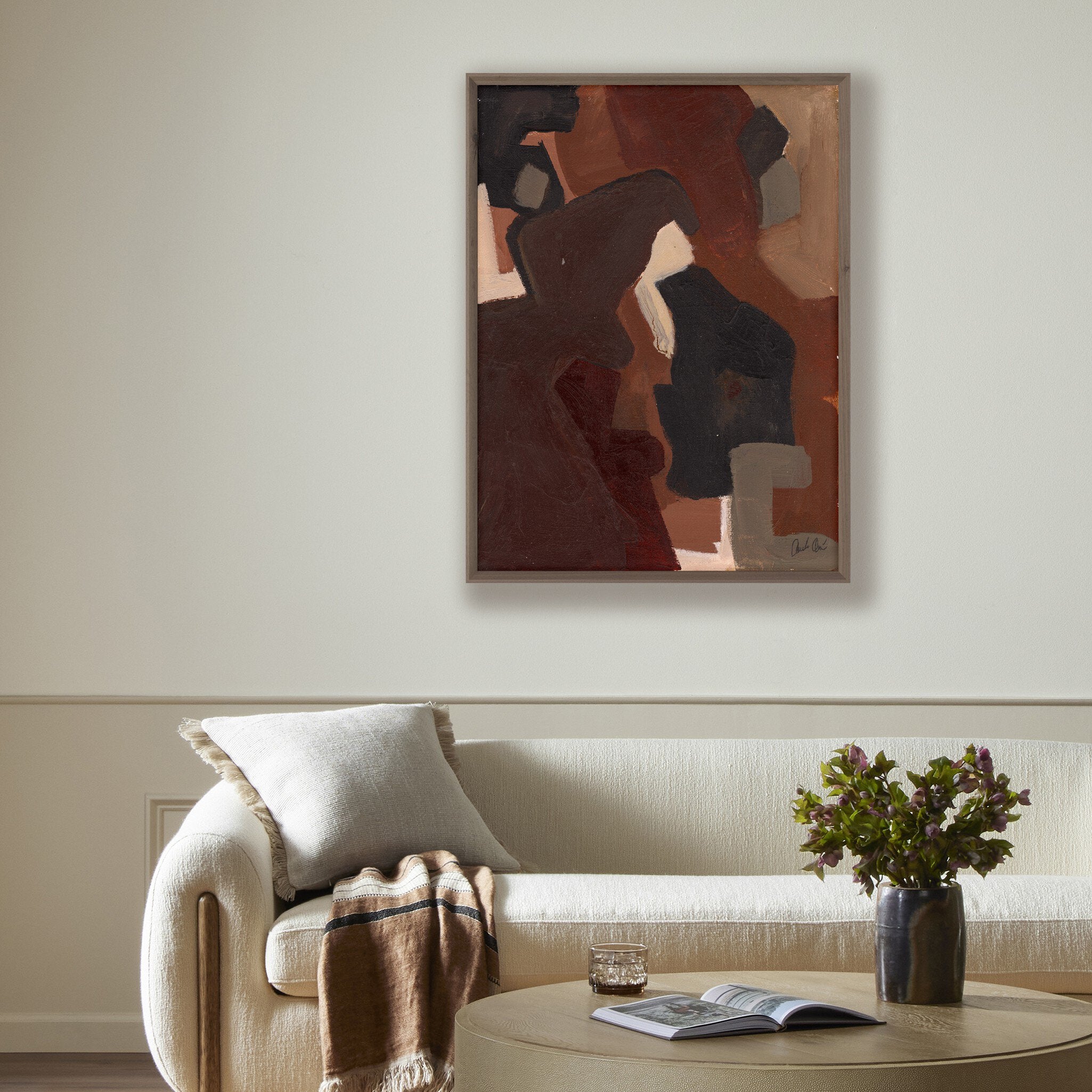 Living room with a beige sofa, abstract painting on the wall, and a small table with a vase and book.