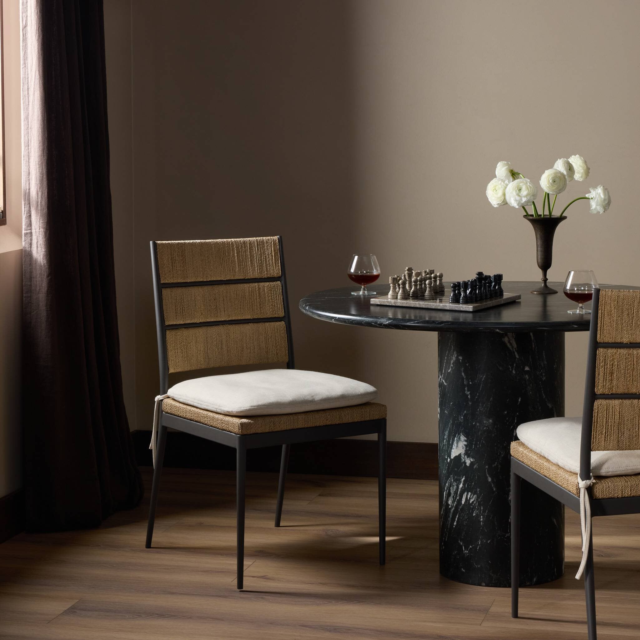 Dining room with a round marble table and two chairs, featuring a vase of flowers and a glass of wine.
