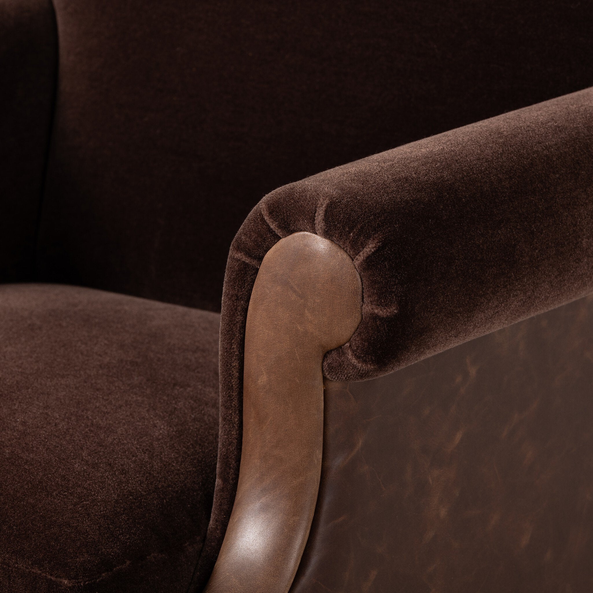 Close-up of a brown velvet armchair with a leather armrest.