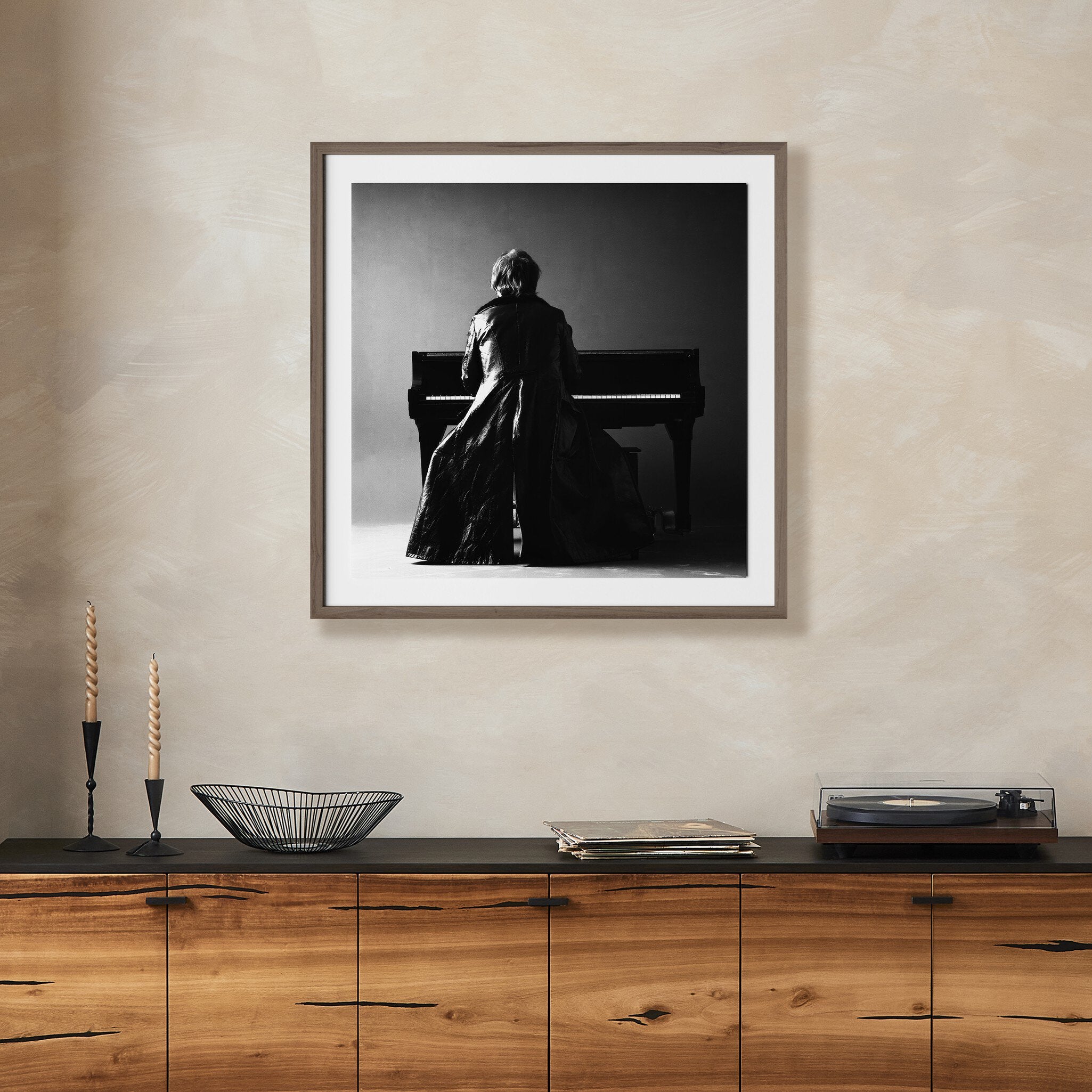Framed black and white artwork of Elton John at a piano on a wall above a wooden cabinet.