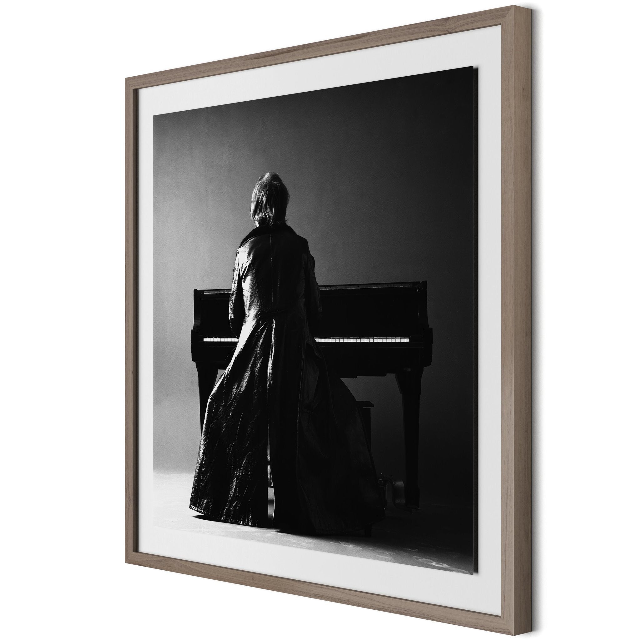 Framed black and white photograph of Elton John in a coat standing by a piano.