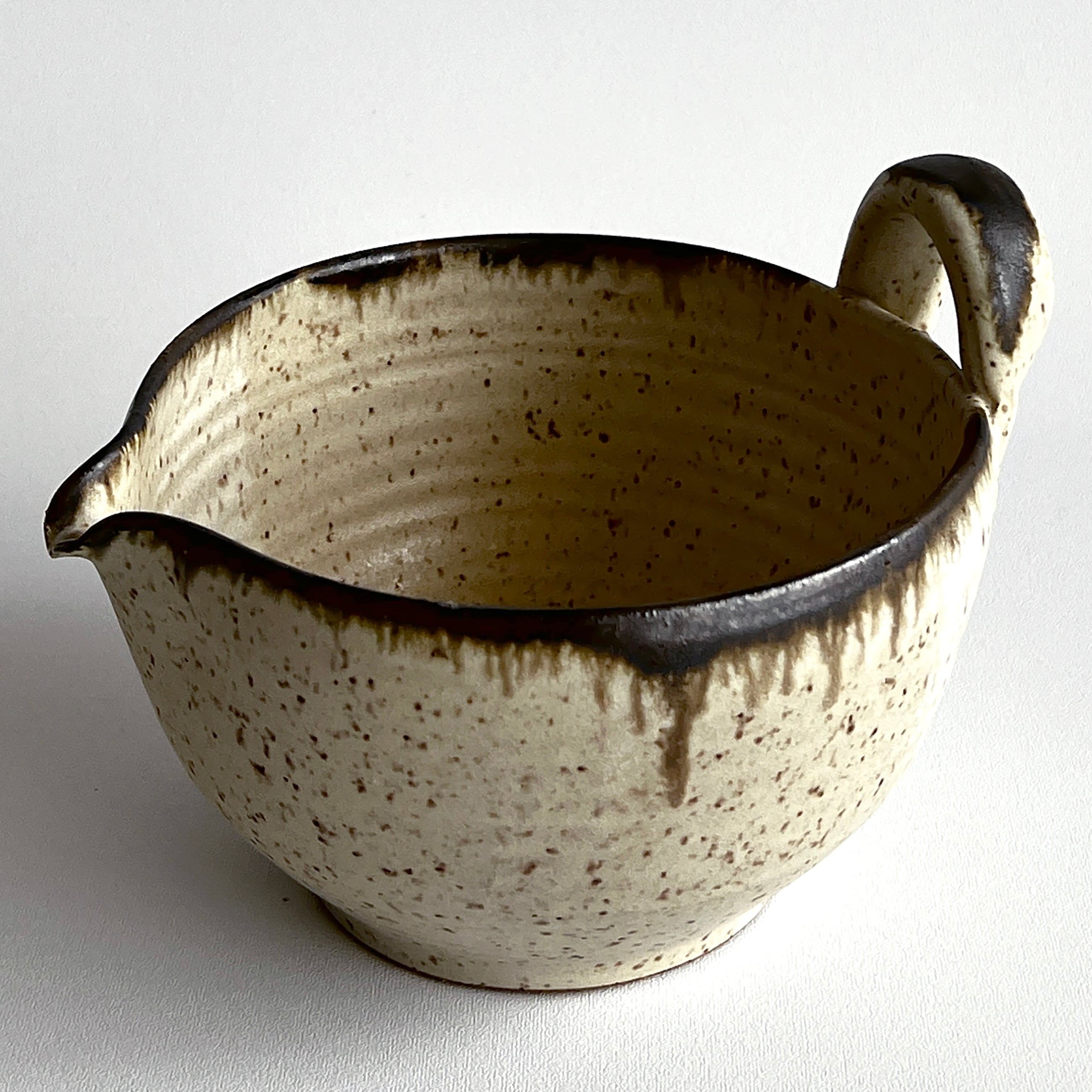 Ceramic pitcher with speckled glaze on a white background