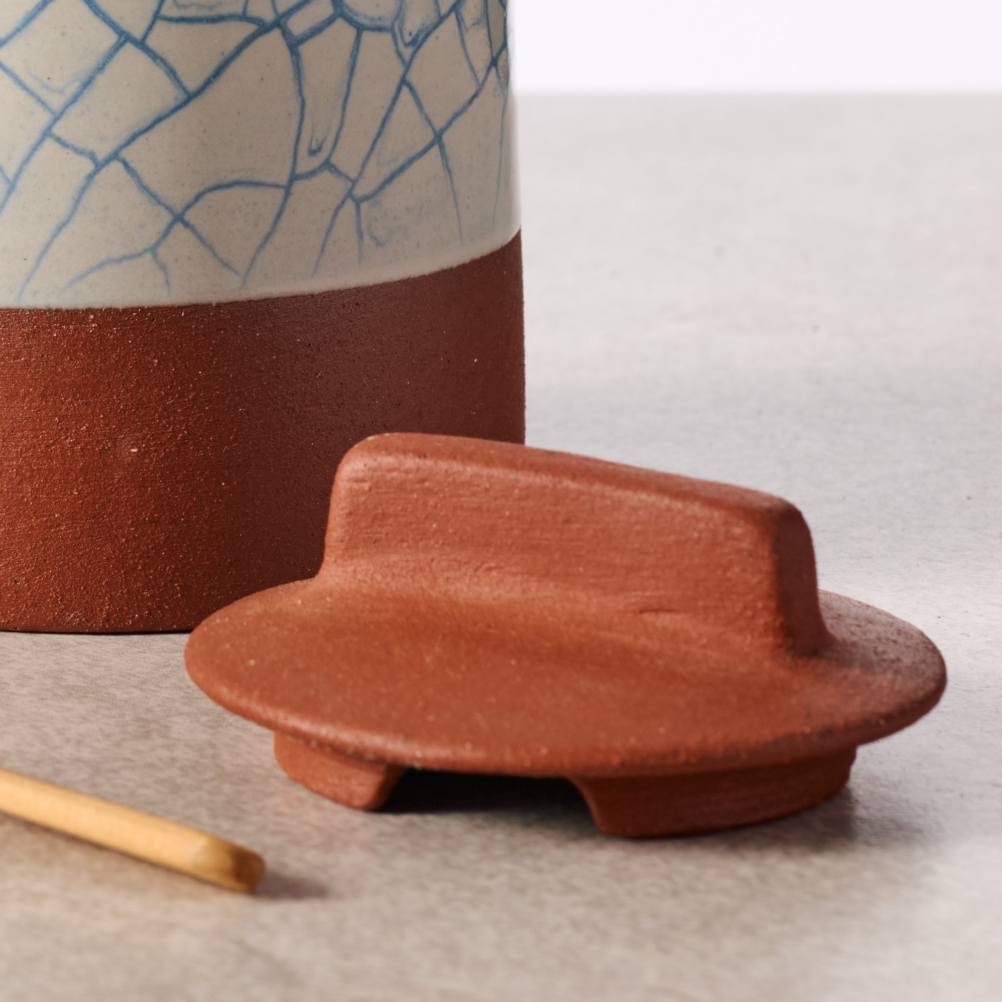 Ceramic jar with a lid and a small wooden tool on a light surface