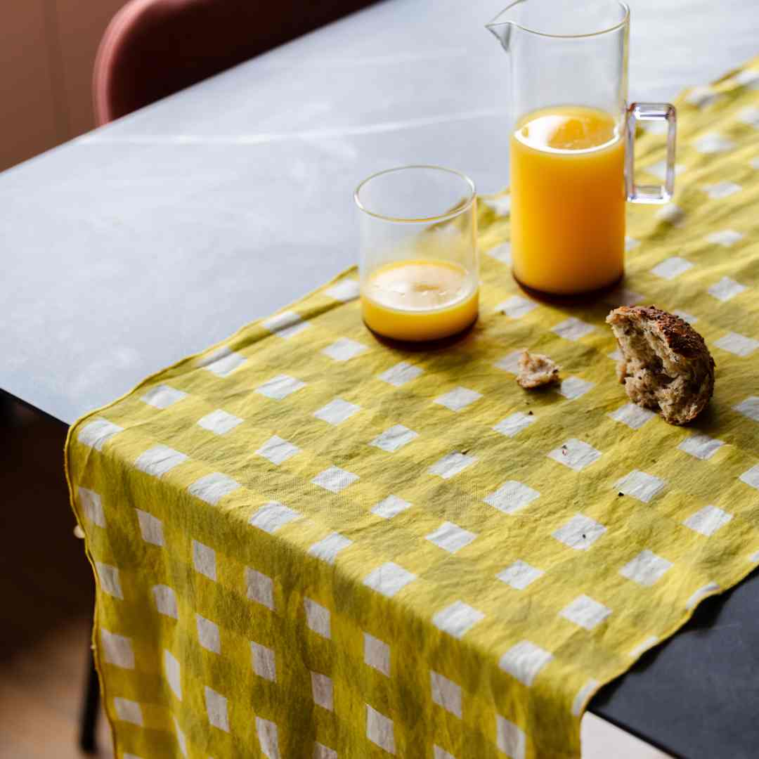 Two glasses of orange juice and a pitcher on a yellow checkered table runner.