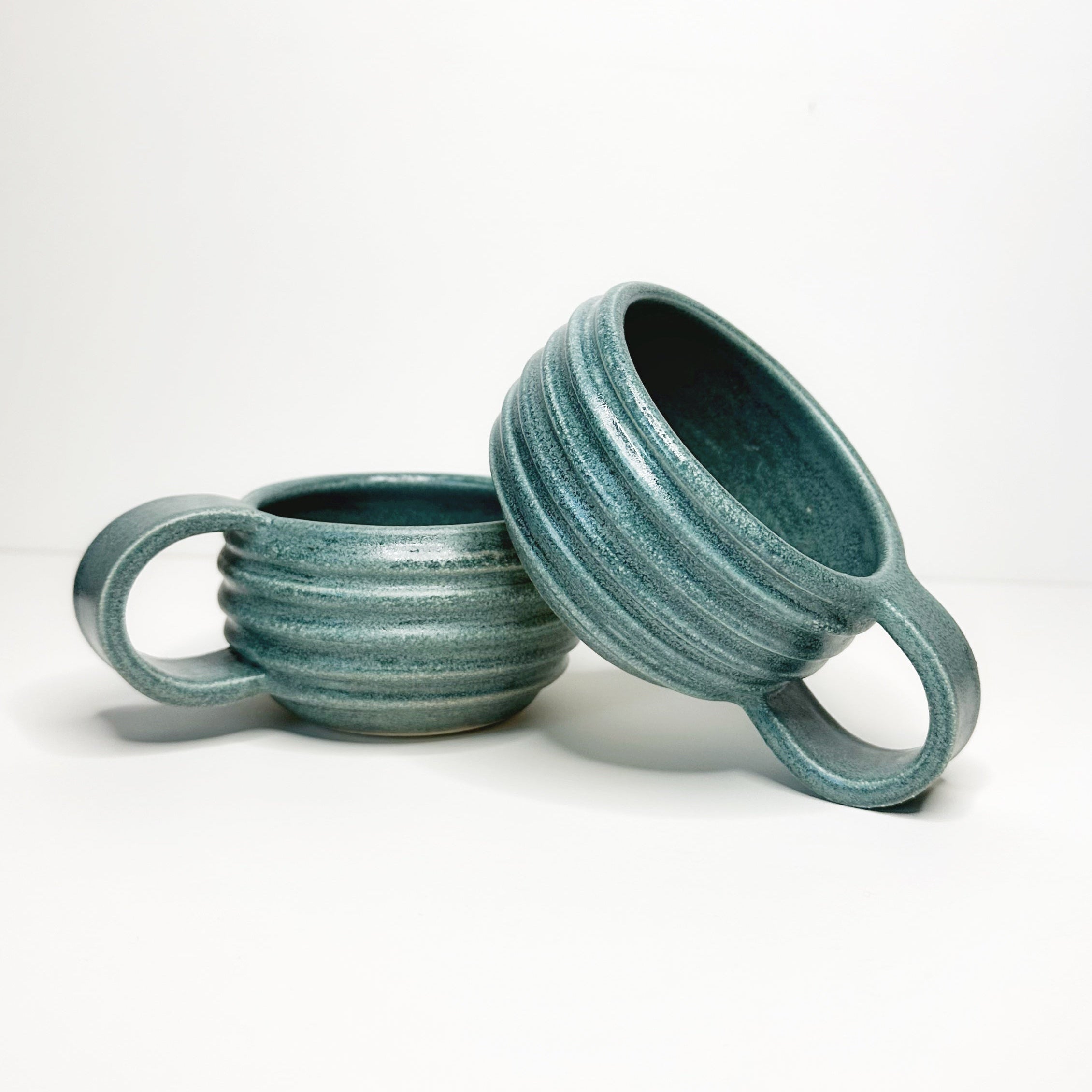 Two teal ceramic mugs with handles on a white background