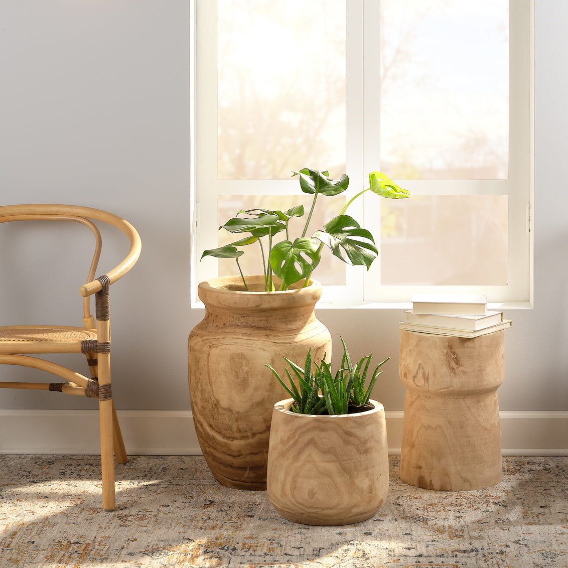Two wooden planters with plants on a rug in front of a window.