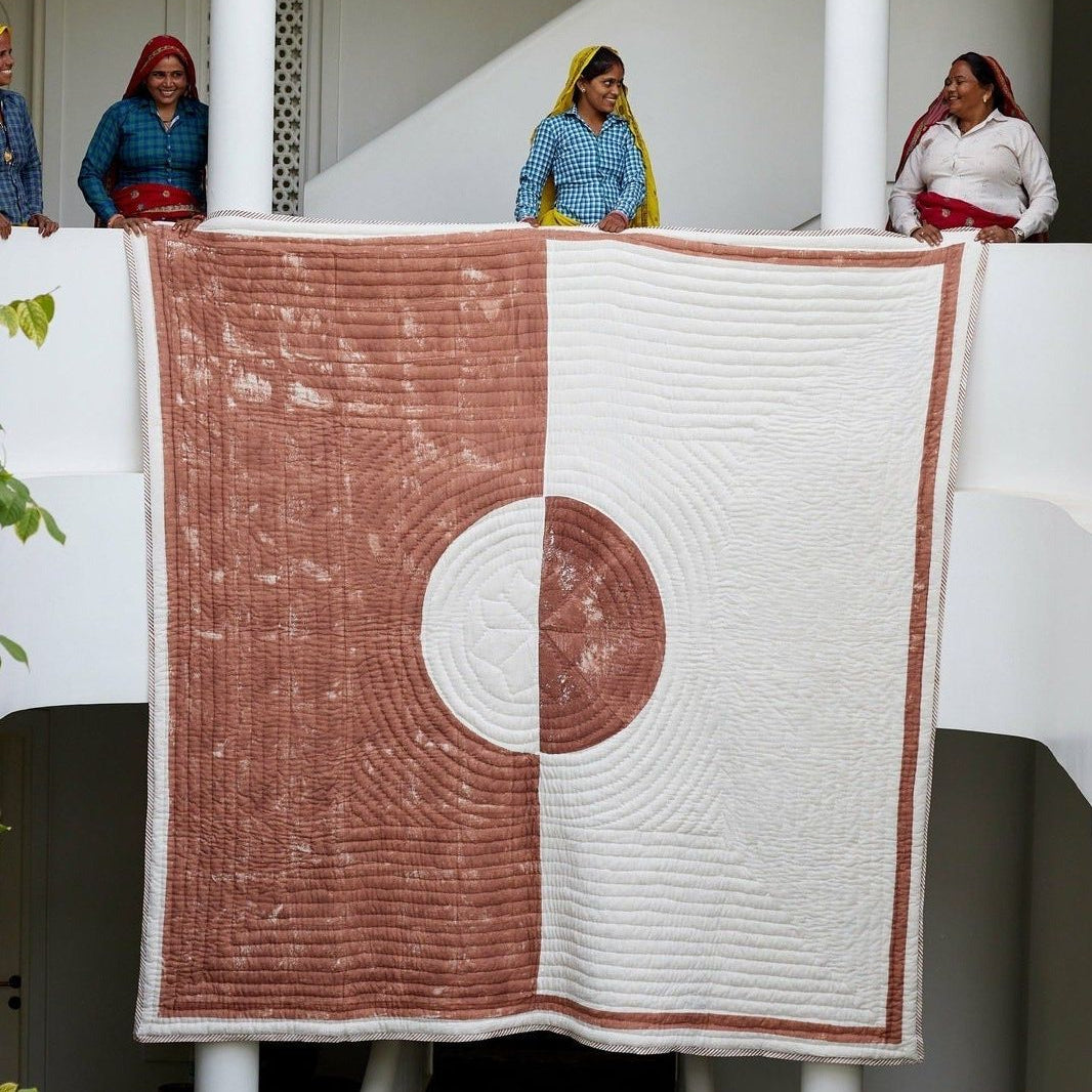 Quilt with circular pattern displayed on a white railing, with people in the background.