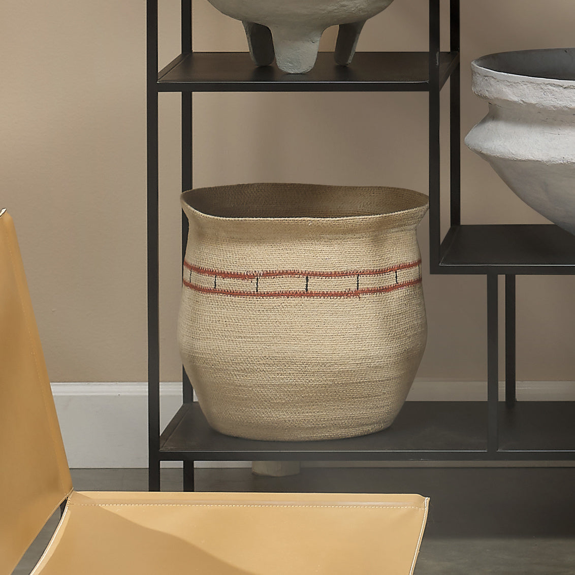 Woven basket with red accents on a black metal shelf against a beige wall.