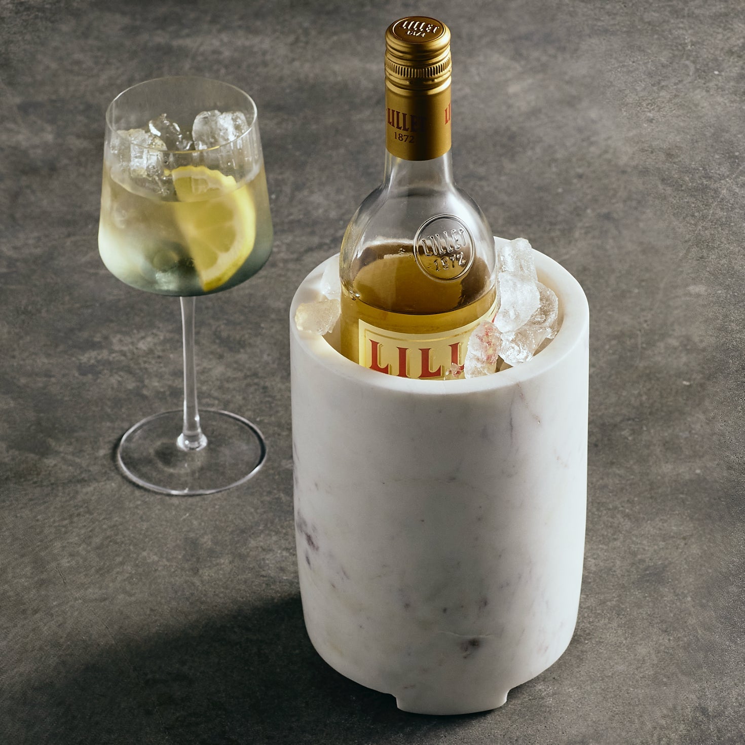Bottle of Lillet in a marble cooler with a glass on a gray surface