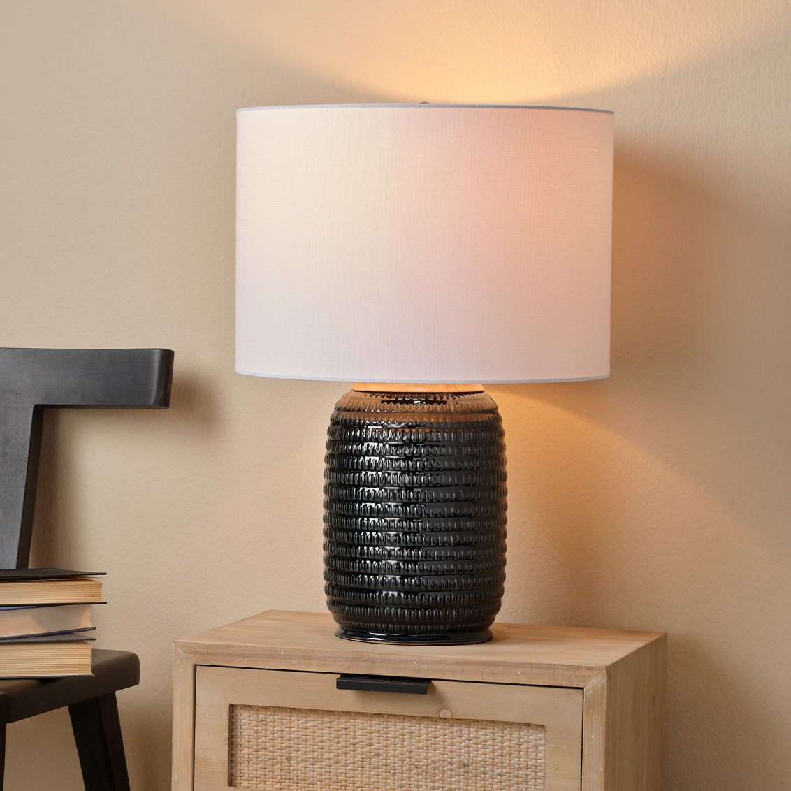 Ceramic table lamp with textured base and white shade on a wooden side table against a beige wall.
