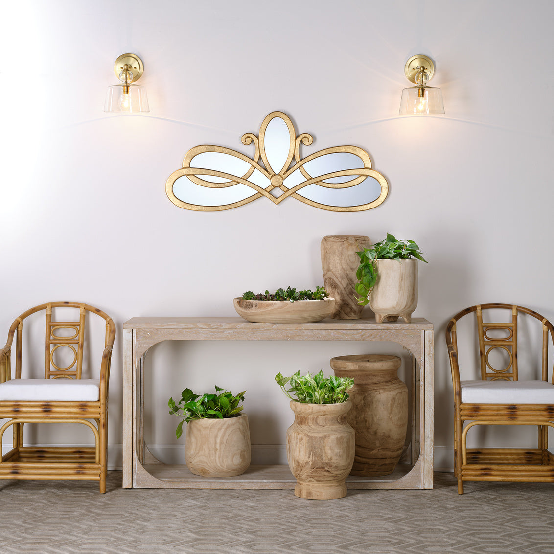 Decorative mirror with floral design above a console table with plants and chairs.