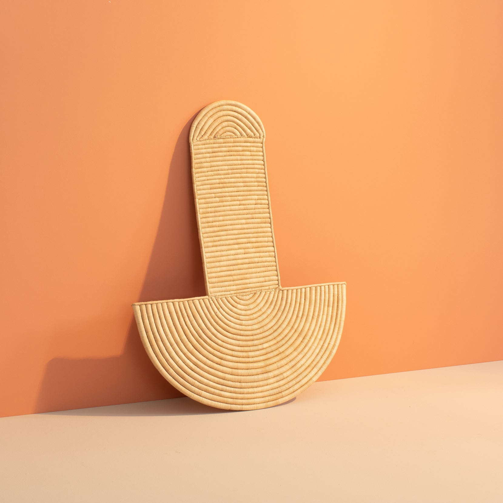 Woven beige wall art piece against an orange background