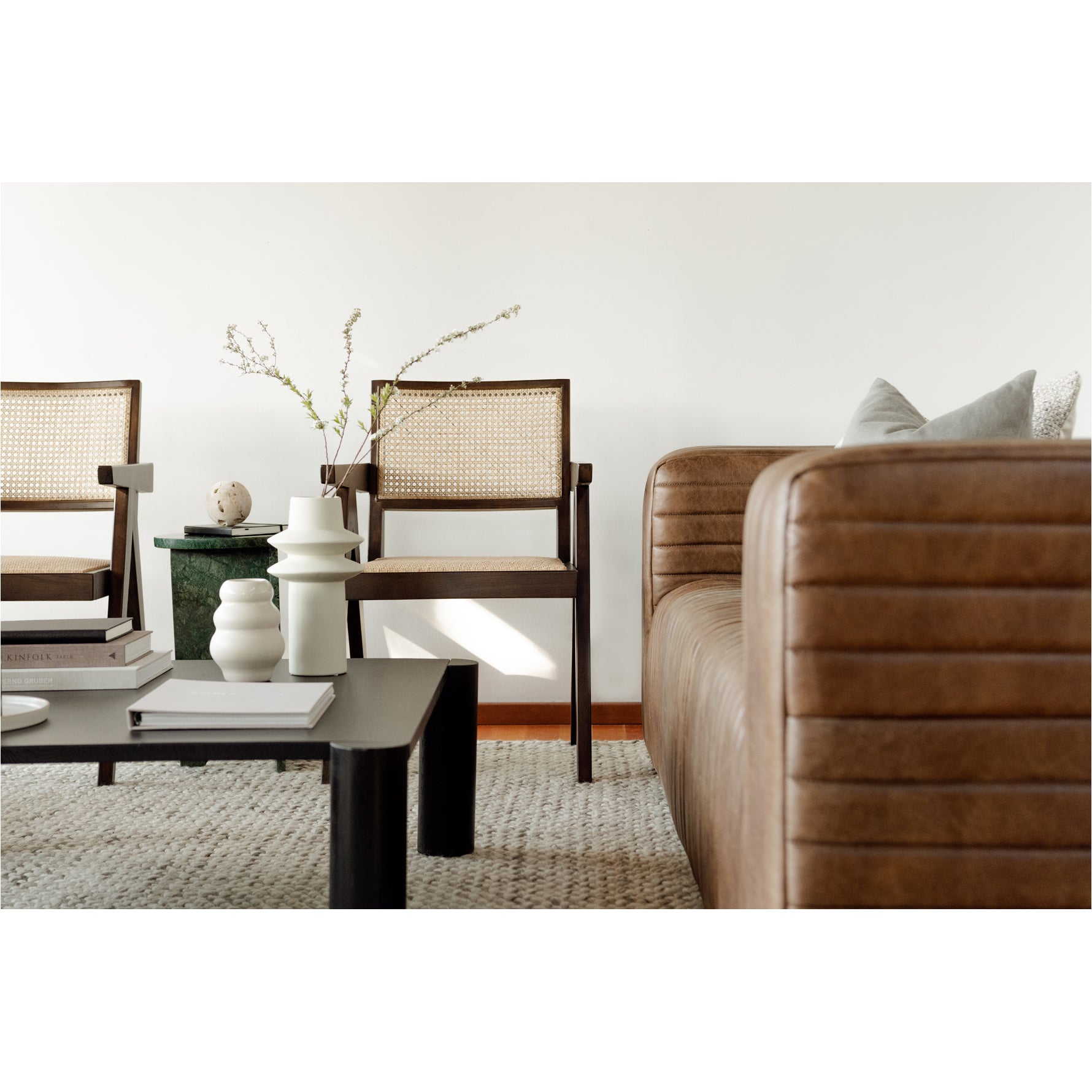 Modern living room with brown leather sofa, wooden chairs, and decorative items.