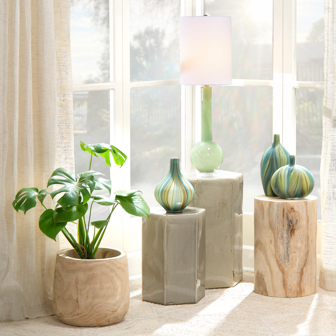 Decorative vases and a plant on small tables in a bright room with large windows.