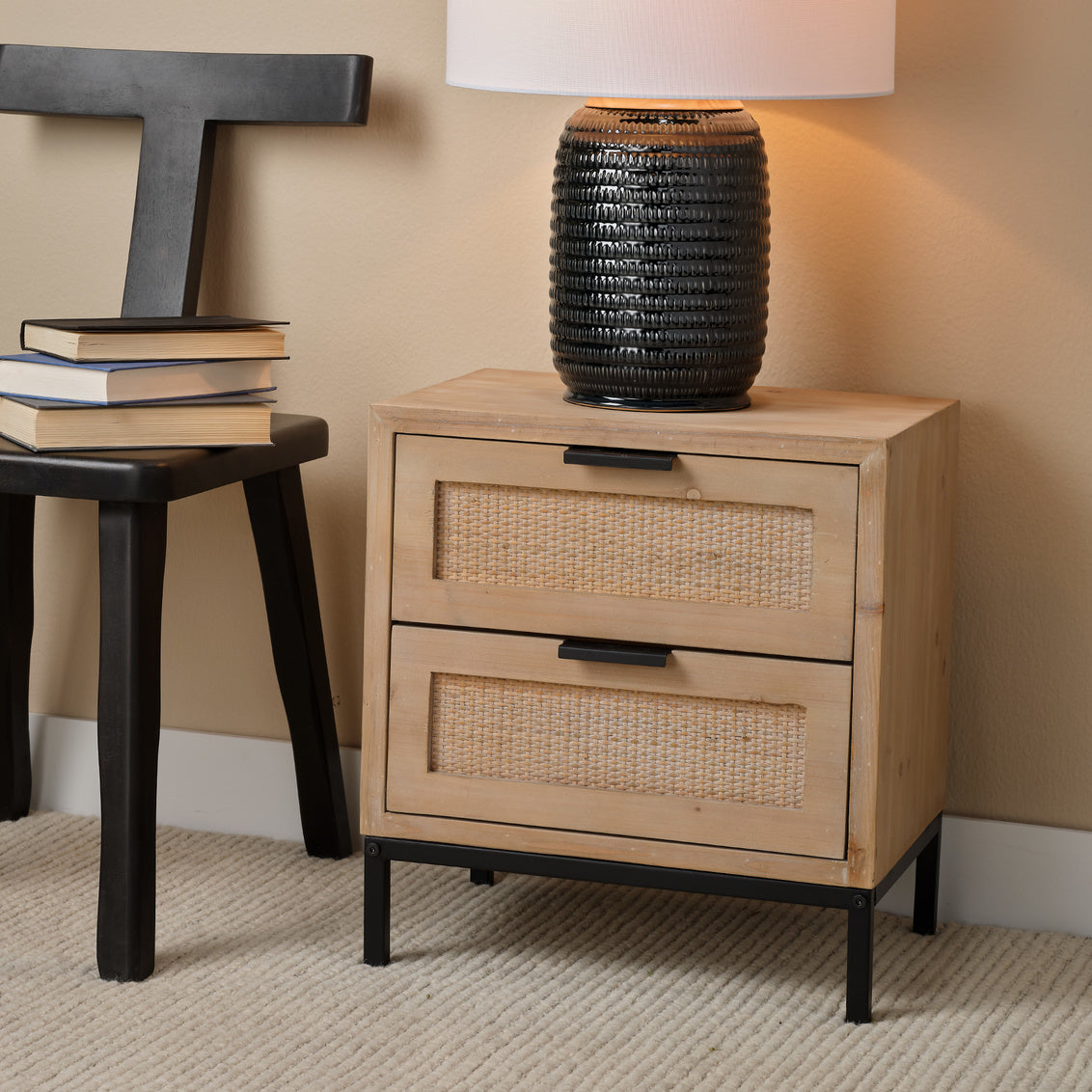 Wooden nightstand with wicker drawers and black lamp on a beige wall background