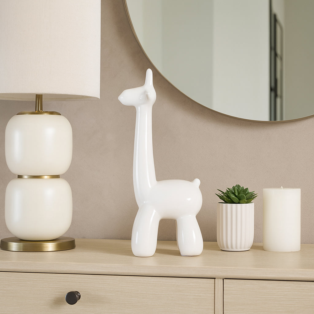 Decorative items including a white ceramic giraffe, lamp, candle, and plant on a wooden surface.