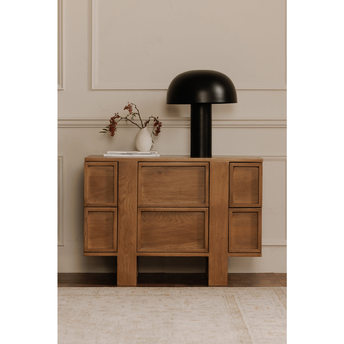 Wooden sideboard with a black lamp and decorative items against a beige wall.