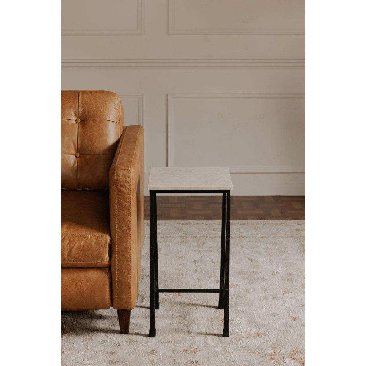 Brown leather armchair next to a small black metal table against a beige paneled wall.