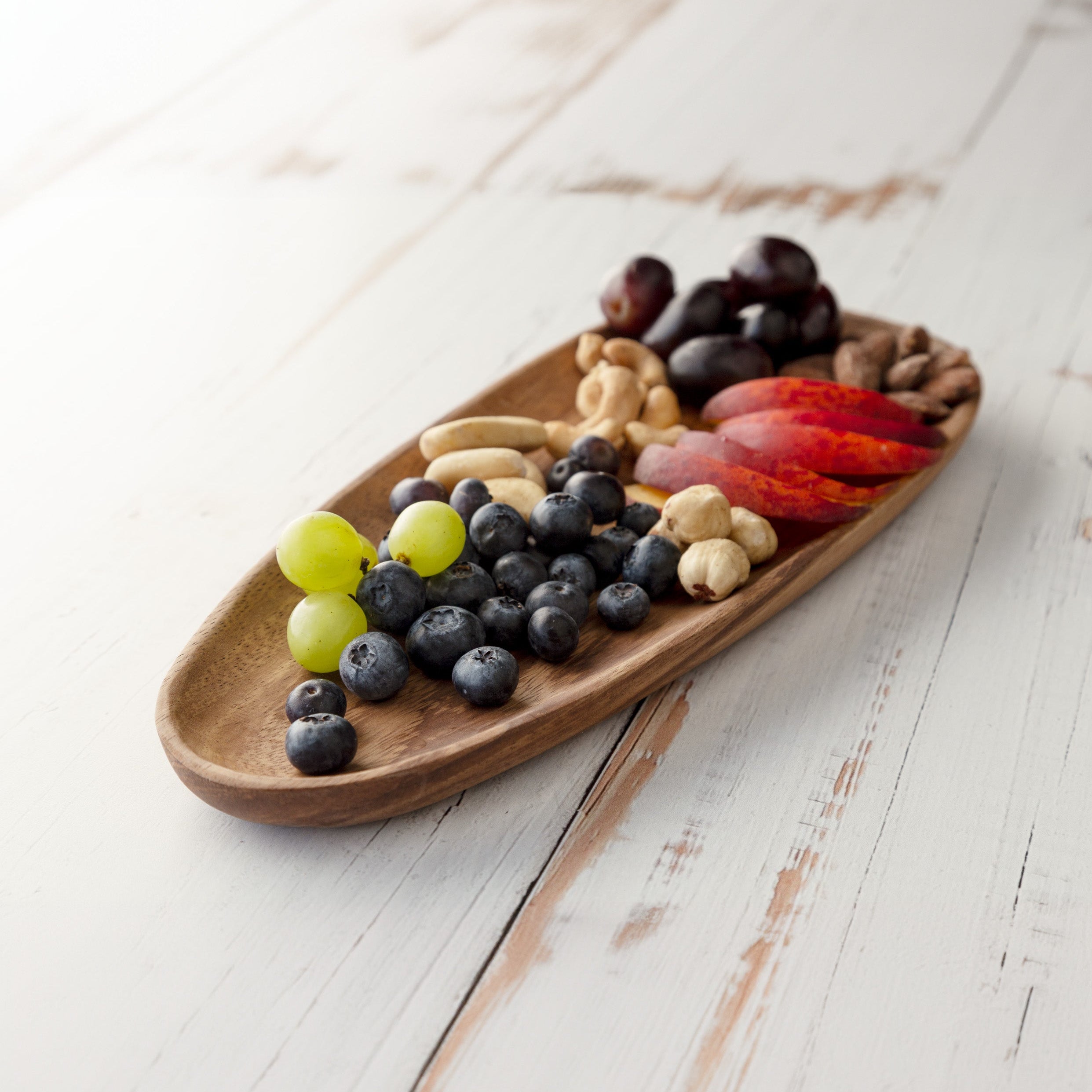 Wooden tray with assorted nuts and fruits on a light wooden surface
