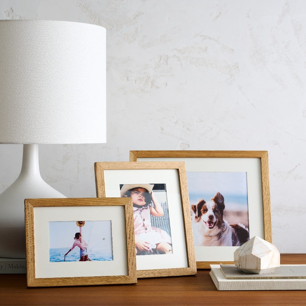 Three wooden picture frames with photos on a table next to a lamp.