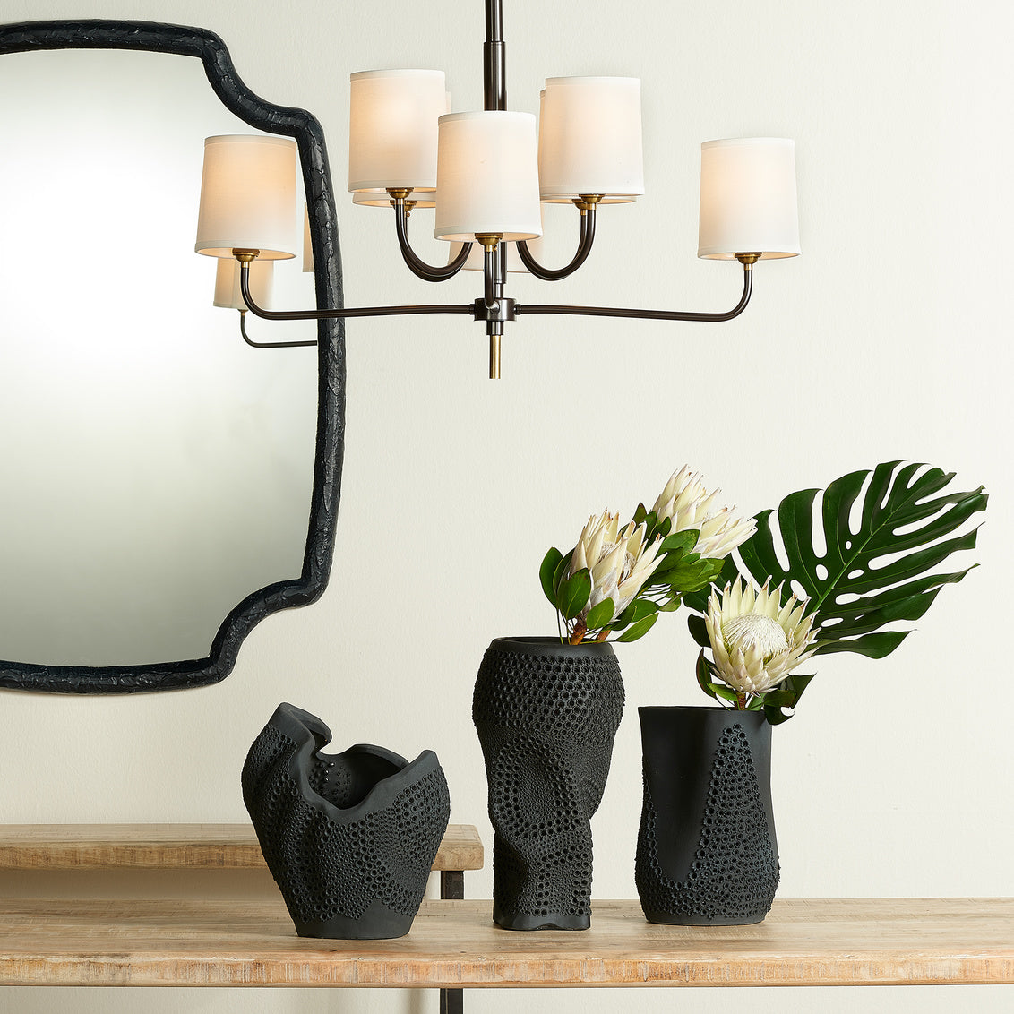 Black textured vases on a wooden surface with a chandelier in the background