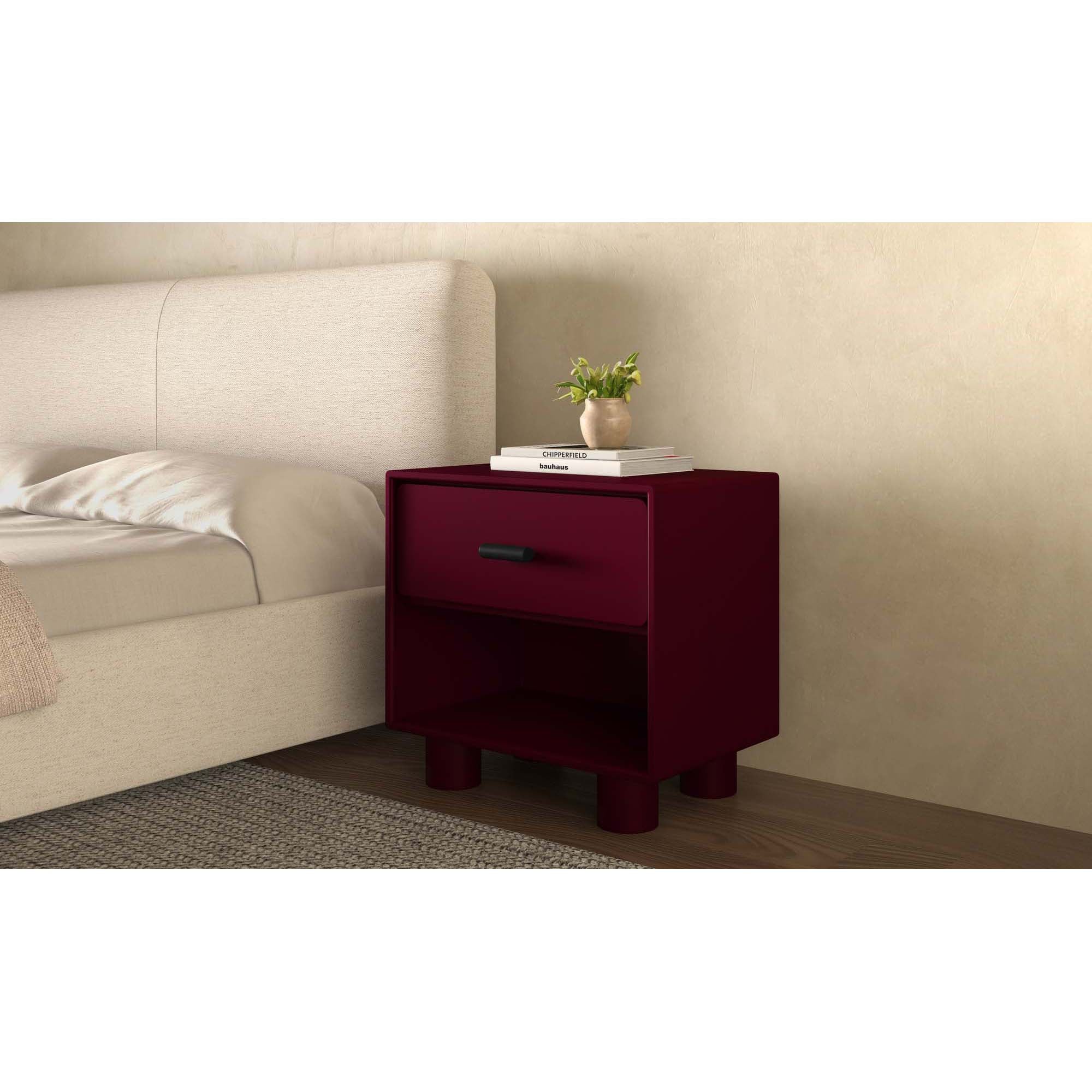 Burgundy nightstand with a plant and books next to a bed in a bedroom setting.