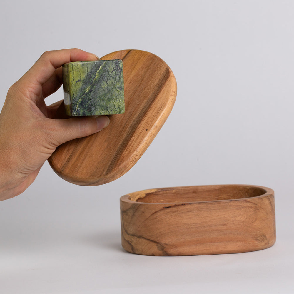 Wooden box with a lid being held open by a hand, revealing a stone inside.