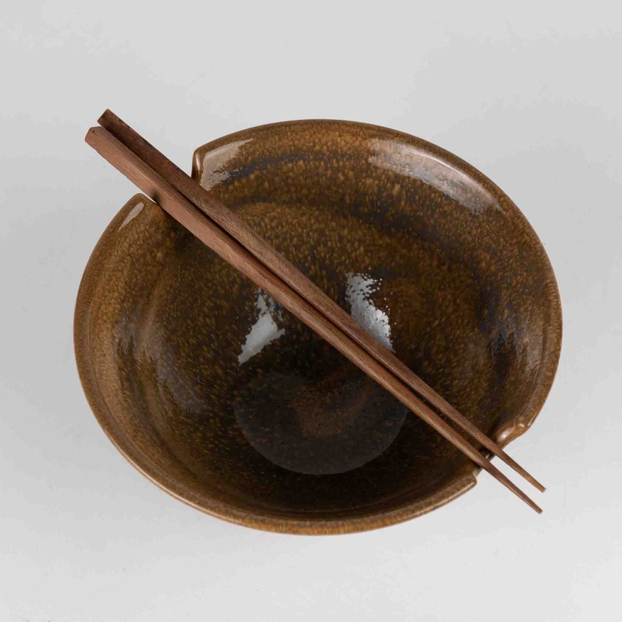 Brown ceramic bowl with a matching spoon on a light gray background