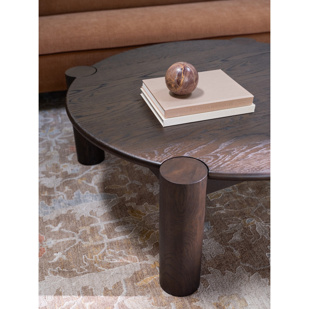 Round wooden coffee table with a marble sphere and books on a patterned rug