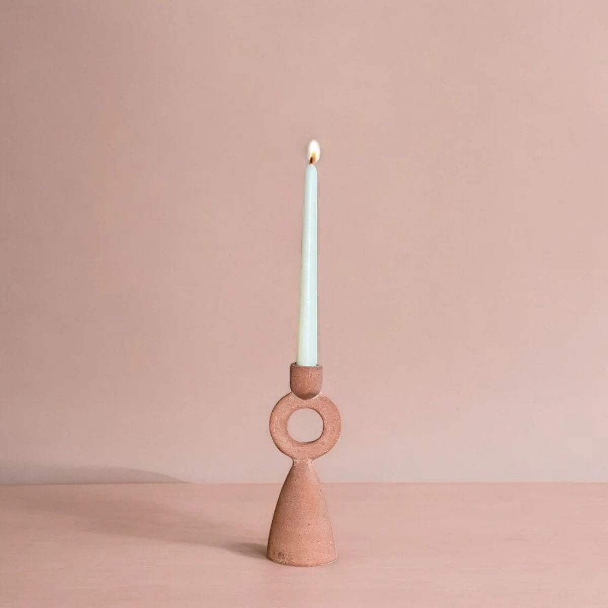 Terracotta candle holder with a lit candle on a beige background