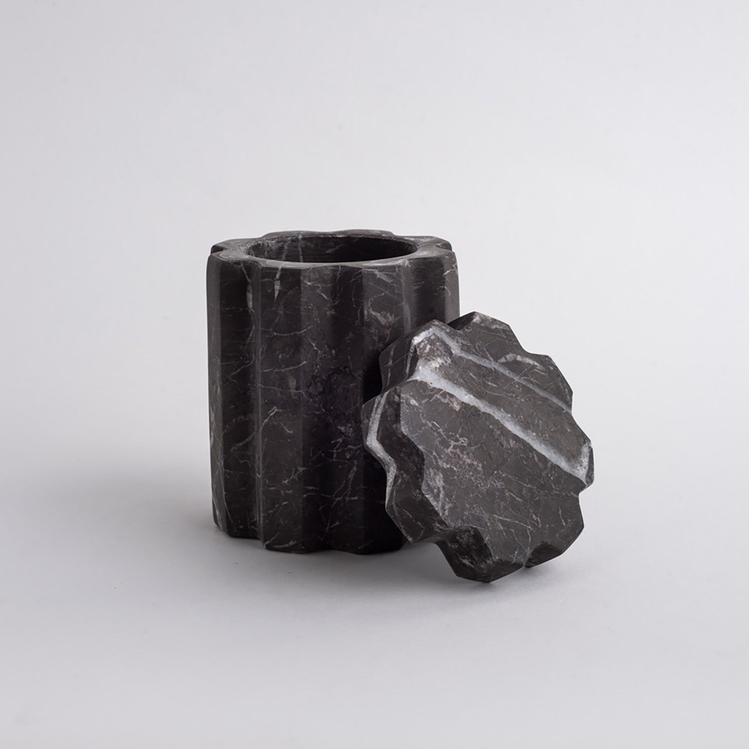 Black stone cylindrical container with a textured surface on a light gray background