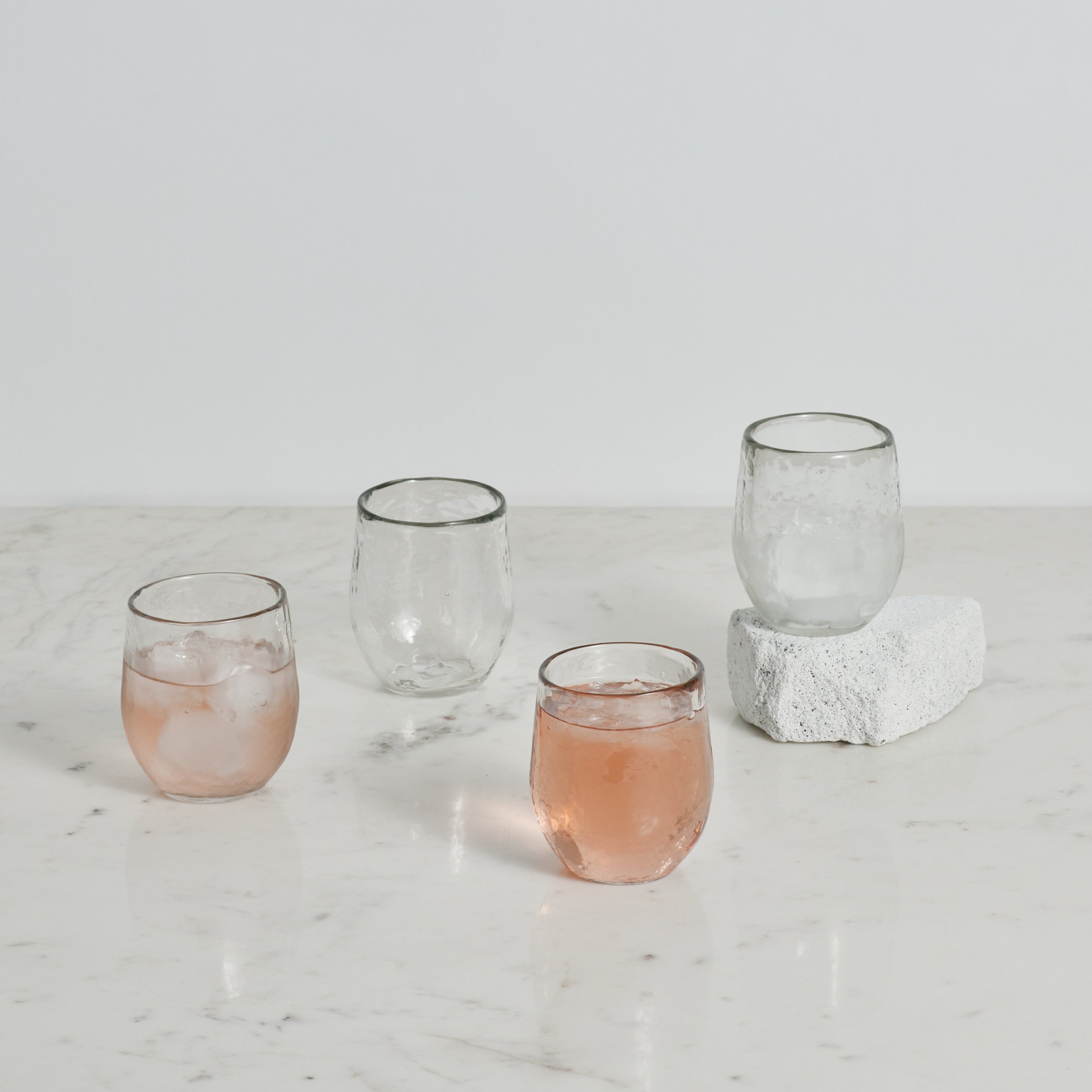 Clear pebbled glasses with pink liquid on a marble surface