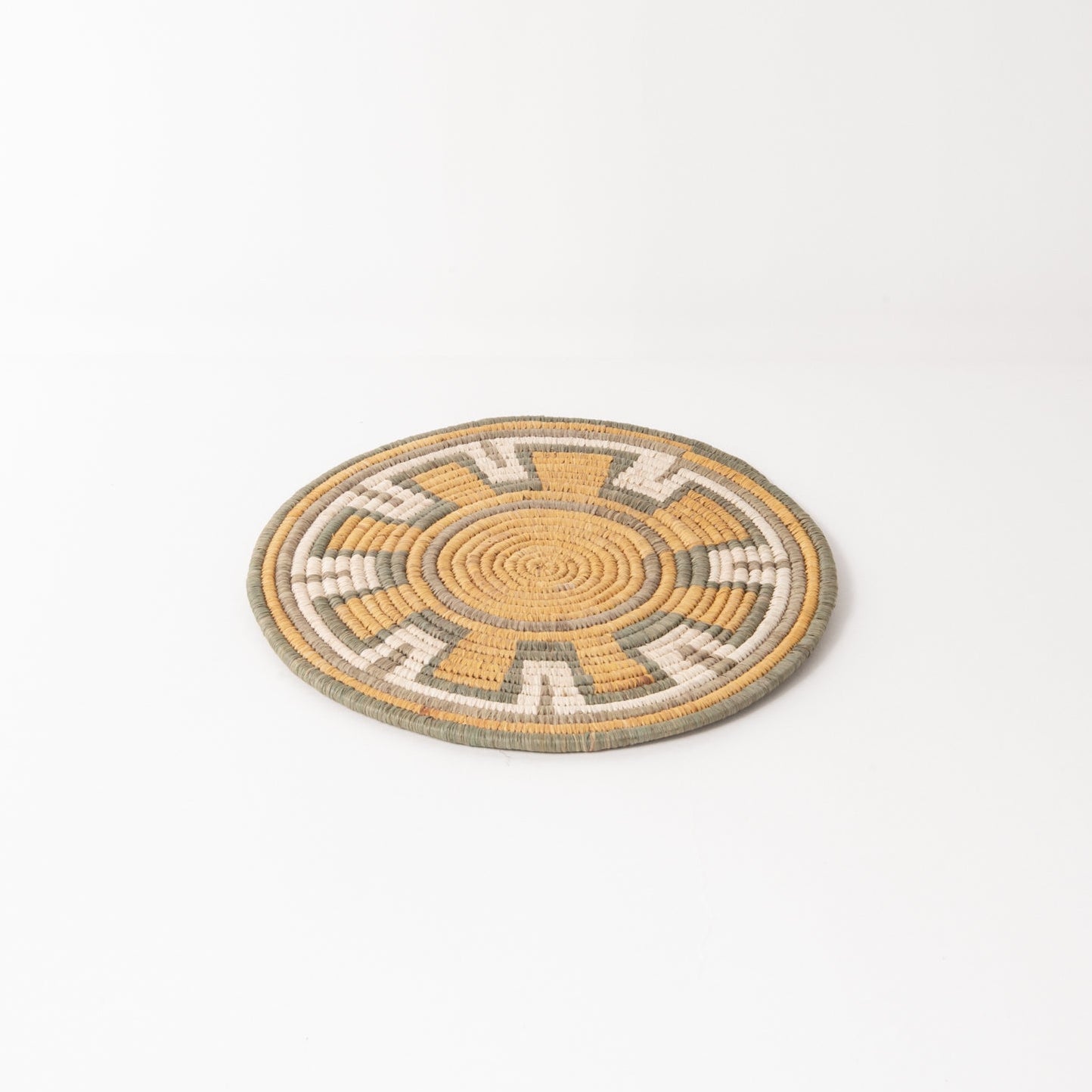 Round woven mat trivet with a geometric pattern on a white background