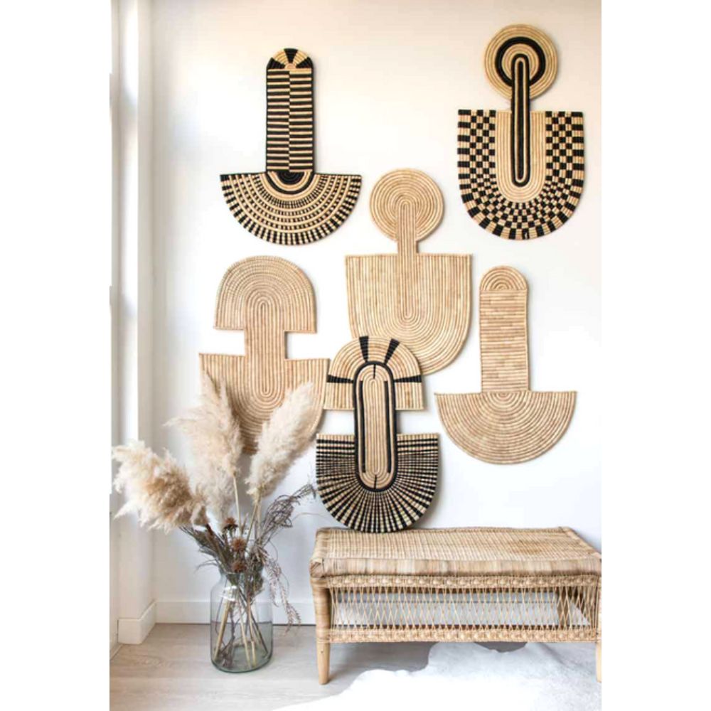 Decorative wall art with geometric patterns on a white wall, accompanied by a woven bench and vase with dried plants.