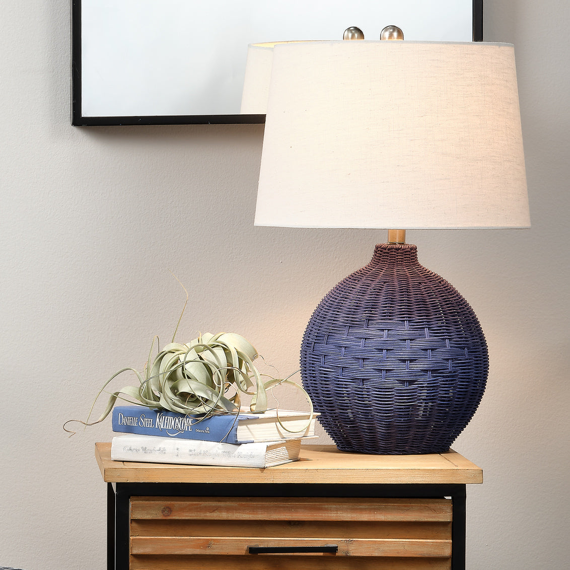 Table lamp with indigo rattan design on a wooden side table against a neutral wall.