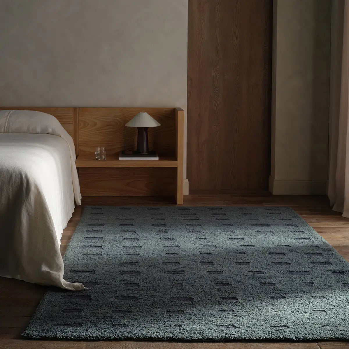 Bedroom with a wooden headboard and nightstand featuring a lamp, with a green rug on the floor.