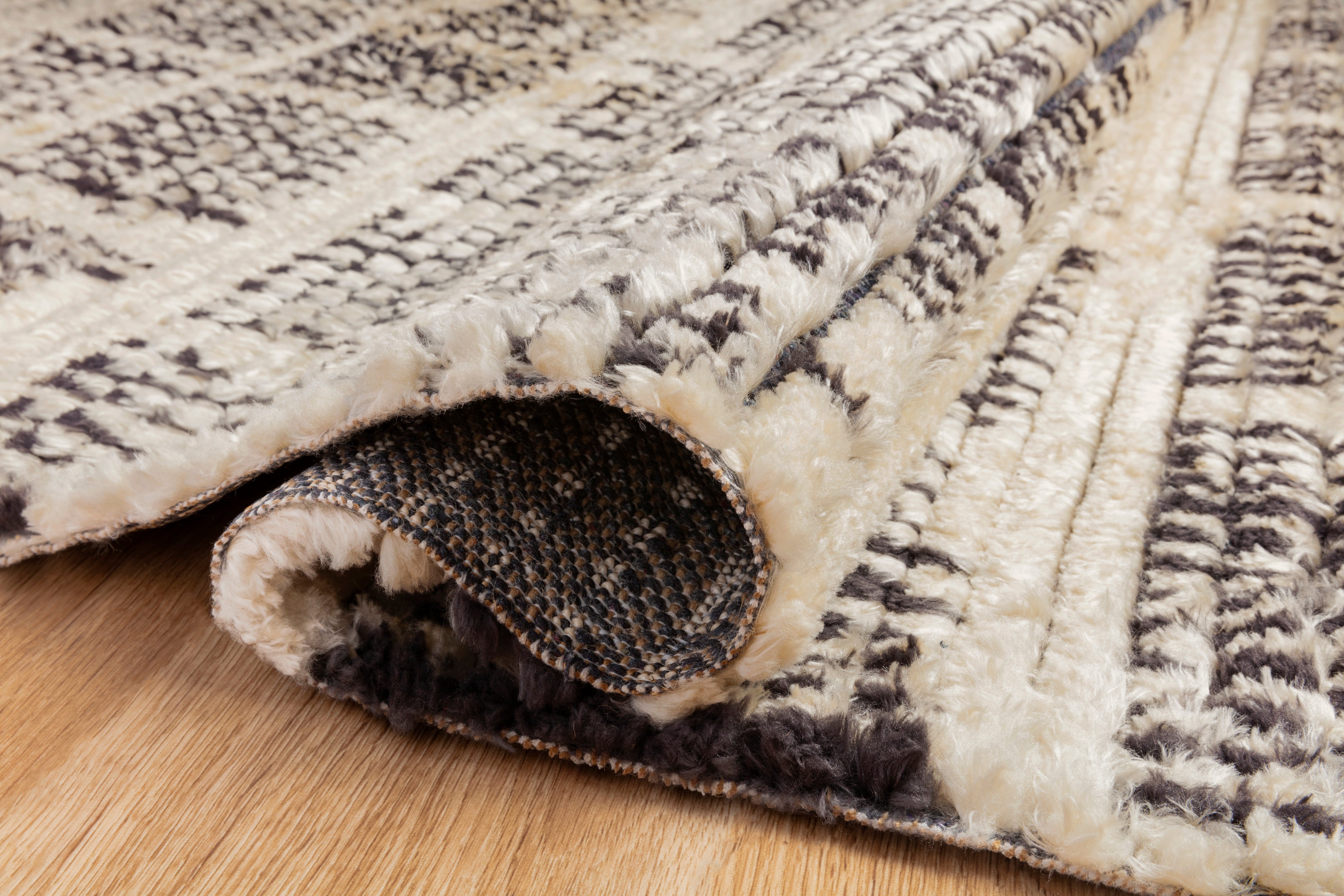 A rectangular rug with a geometric pattern featuring a combination of black and gray colors, with subtle fringes on the edges.