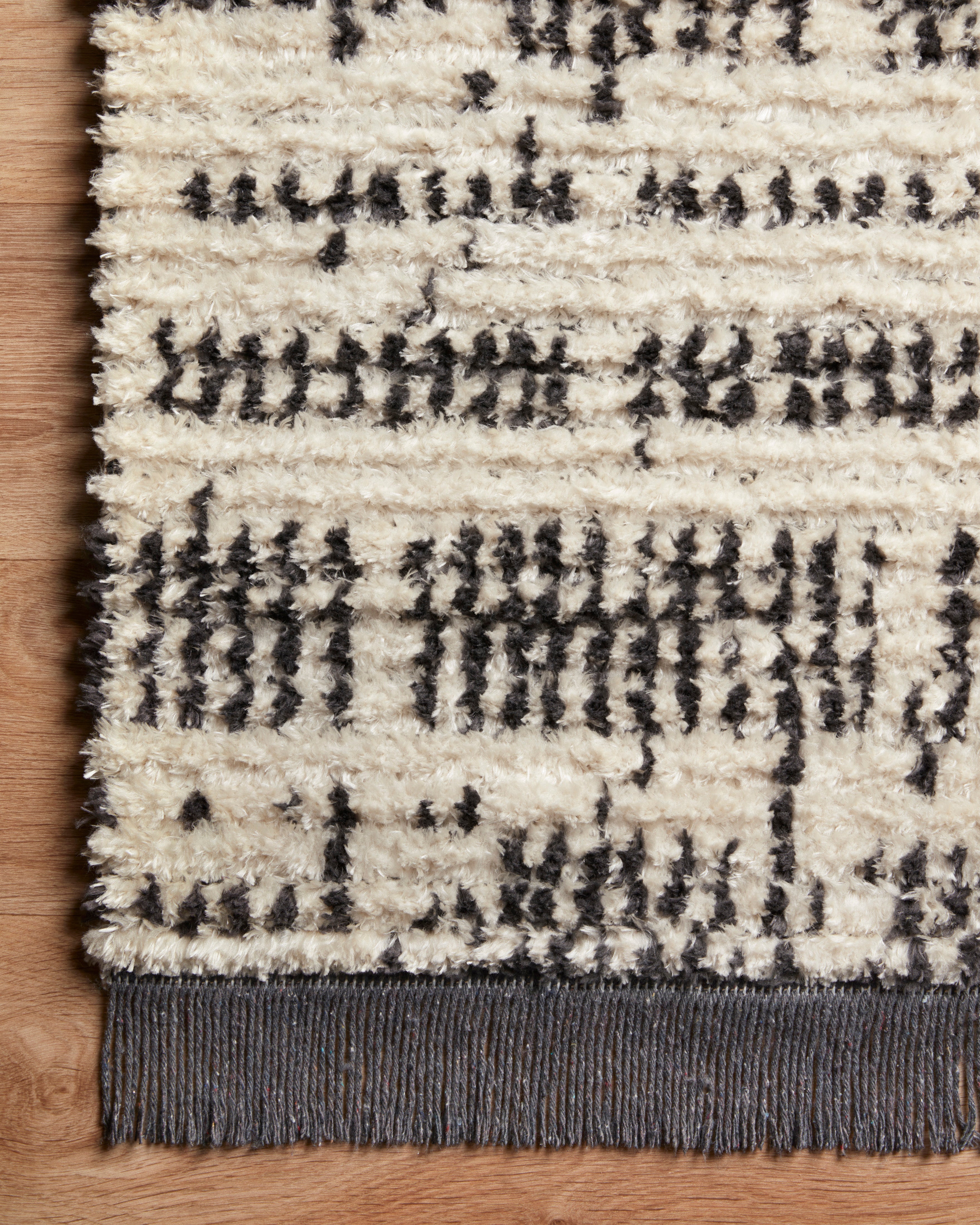 A rectangular rug with a geometric pattern featuring a combination of black and gray colors, with subtle fringes on the edges.