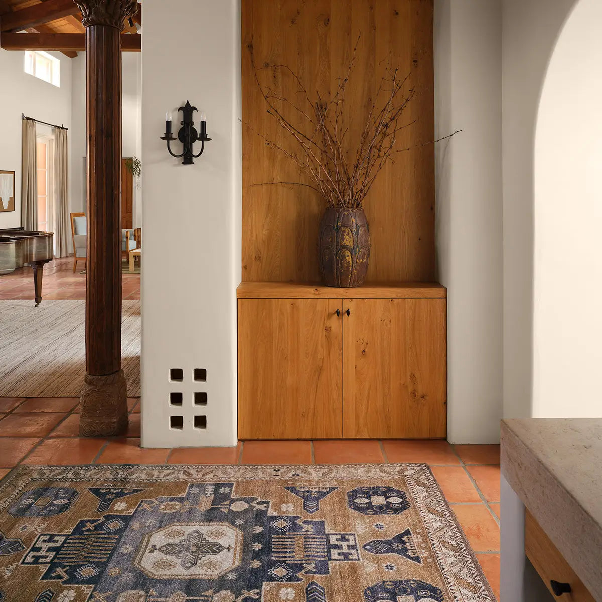 Wooden cabinet with decorative vase against a white wall in a room with a patterned rug.