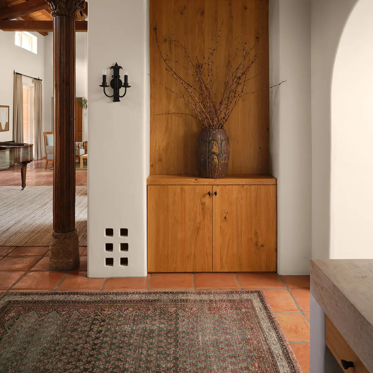 Wooden cabinet with decorative vase and branches in a room with tiled floor and archway.